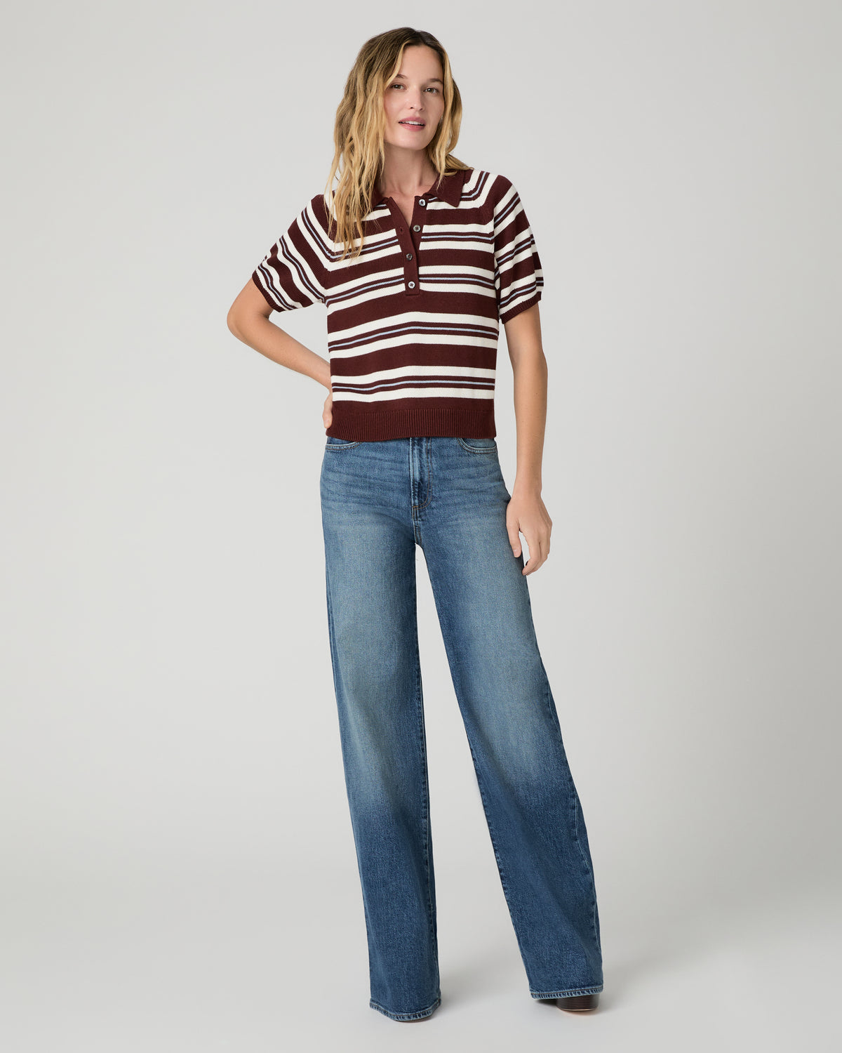 Women wearing a white and brown stripe top and blue jeans paired with brown boots against a white background