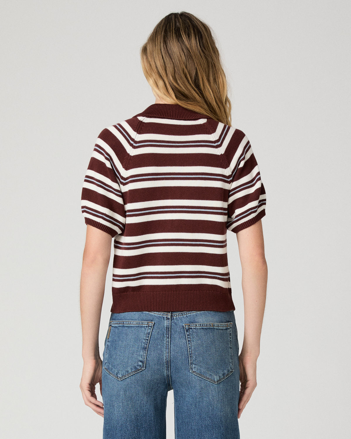 Women wearing a white and brown stripe top and blue jeans against a white background