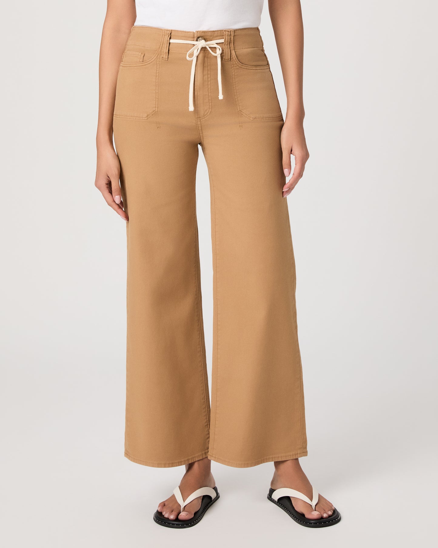 Woman wearing a white t-shirt and tan wide-leg pants paired with white sandals on a white background