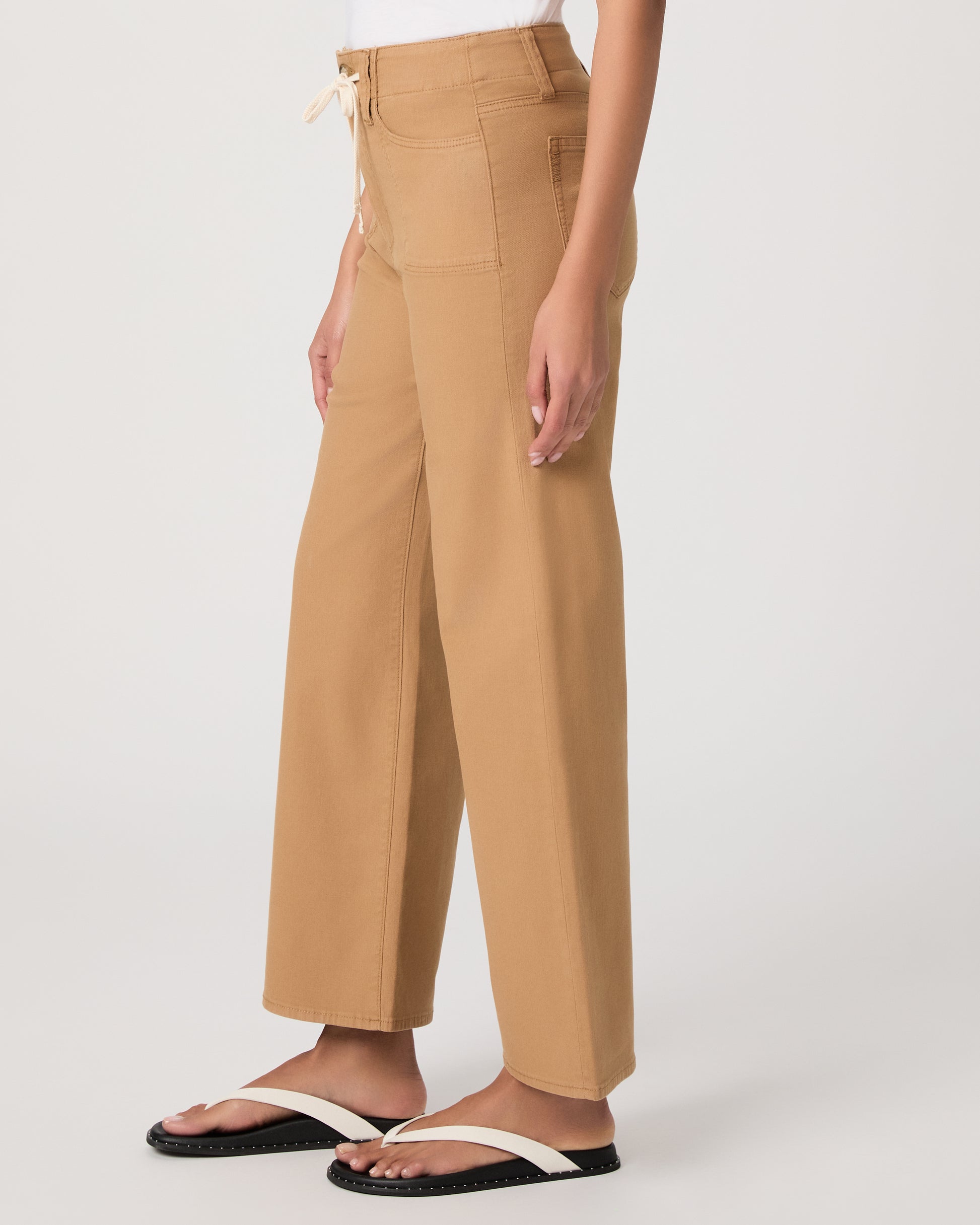 Woman wearing a white t-shirt and tan wide-leg pants paired with white sandals on a white background