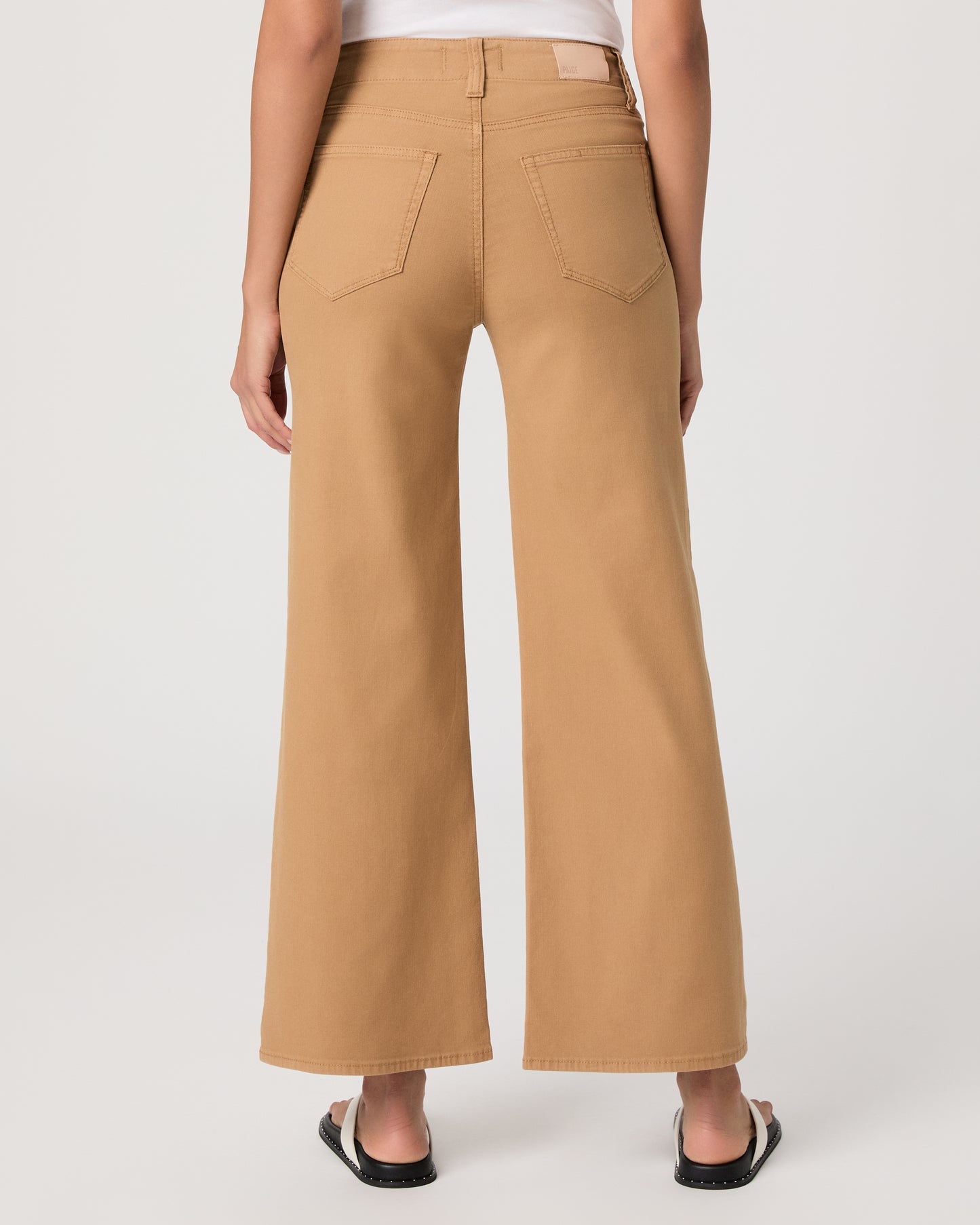 Woman wearing a white t-shirt and tan wide-leg pants paired with white sandals on a white background
