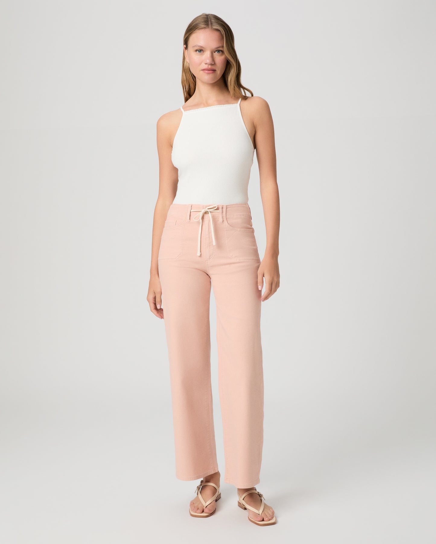 Women wearing a light peach color pant paired with a white tank and sandals against a white background