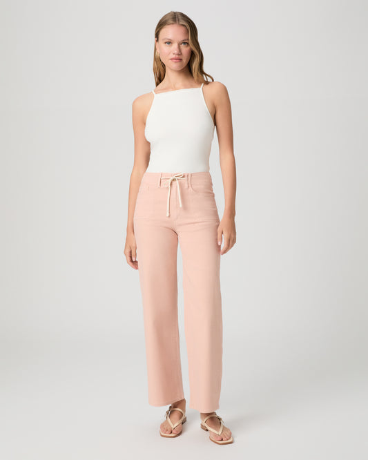 Women wearing a light peach color pant paired with a white tank and sandals against a white background