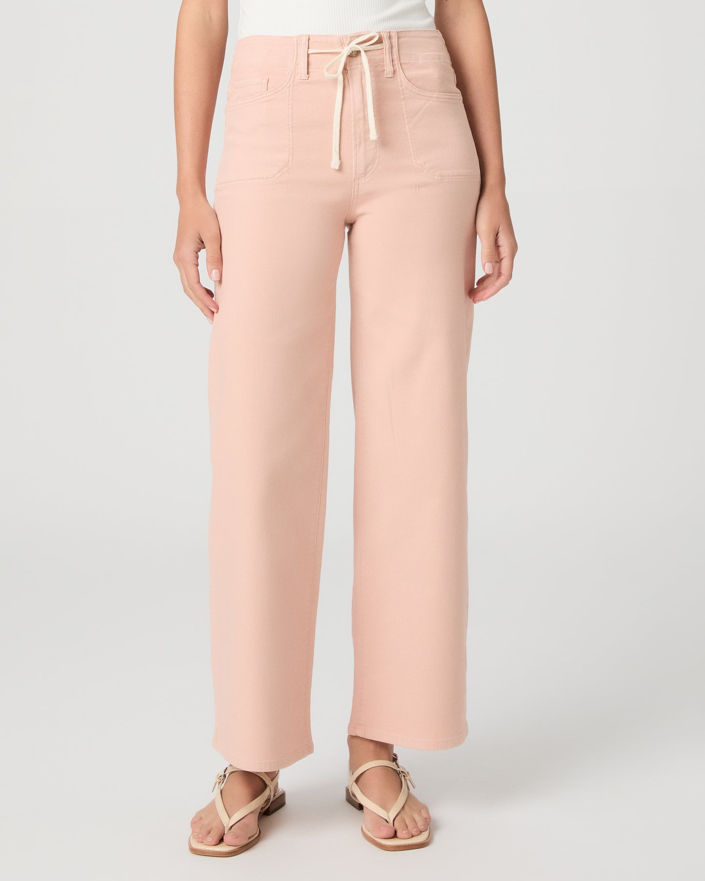 Women wearing a light peach color pant paired with a white tank and sandals against a white background