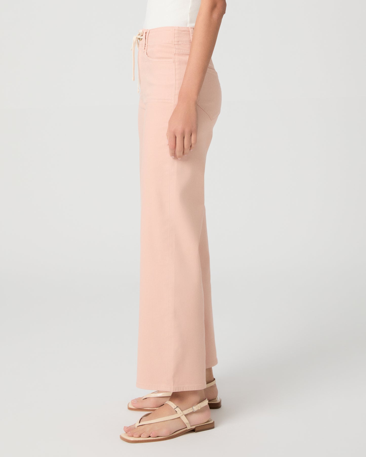 Women wearing a light peach color pant paired with a white tank and sandals against a white background