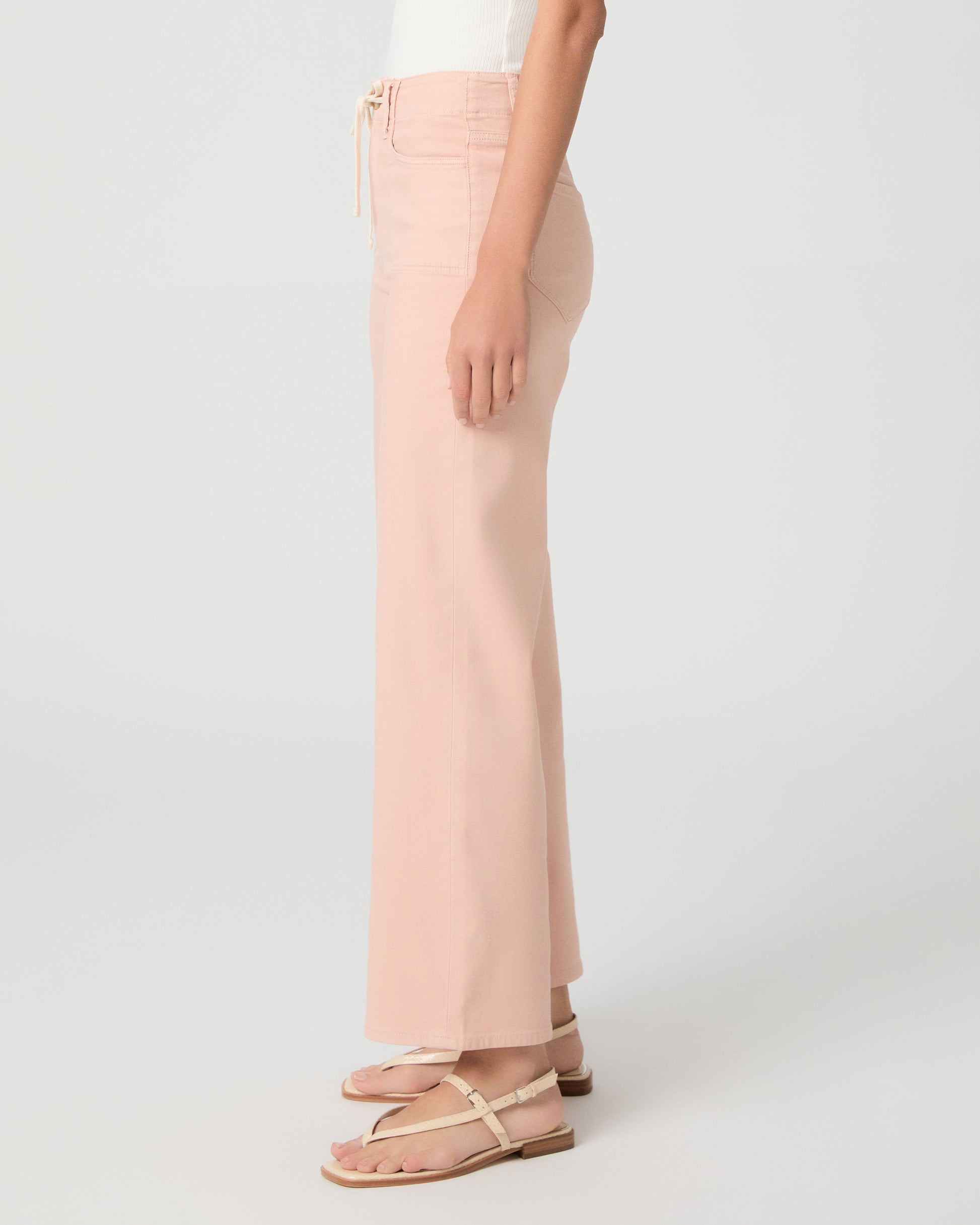 Women wearing a light peach color pant paired with a white tank and sandals against a white background
