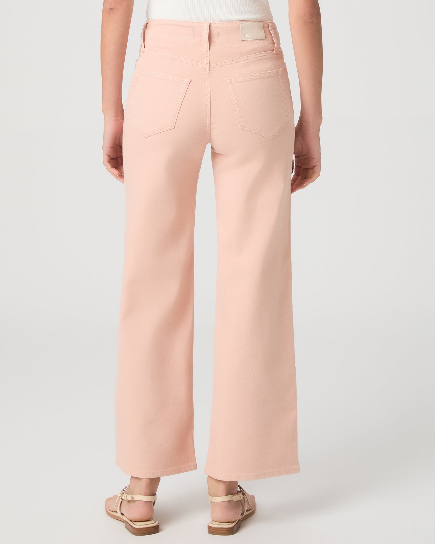 Women wearing a light peach color pant paired with a white tank and sandals against a white background