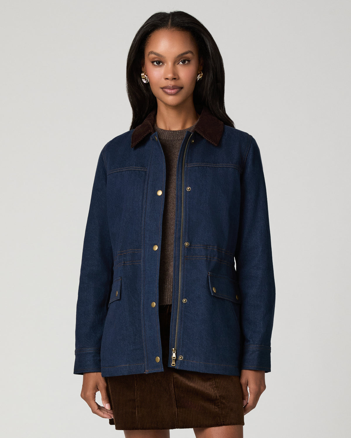 Close-up front view of a woman in a dark denim barn jacket with a brown corduroy collar and snap-front placket, worn over a dark top.