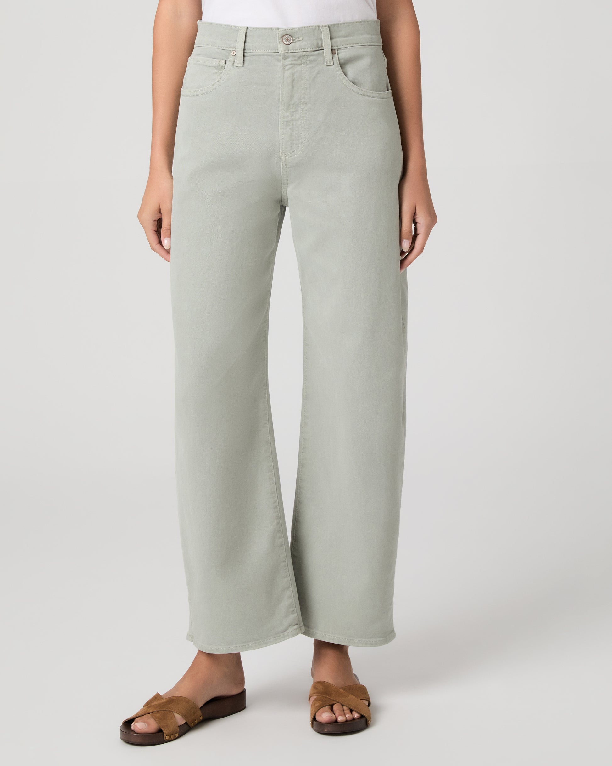 Woman wearing a white t-shirt and light green pants paired with brown sandals on a white background