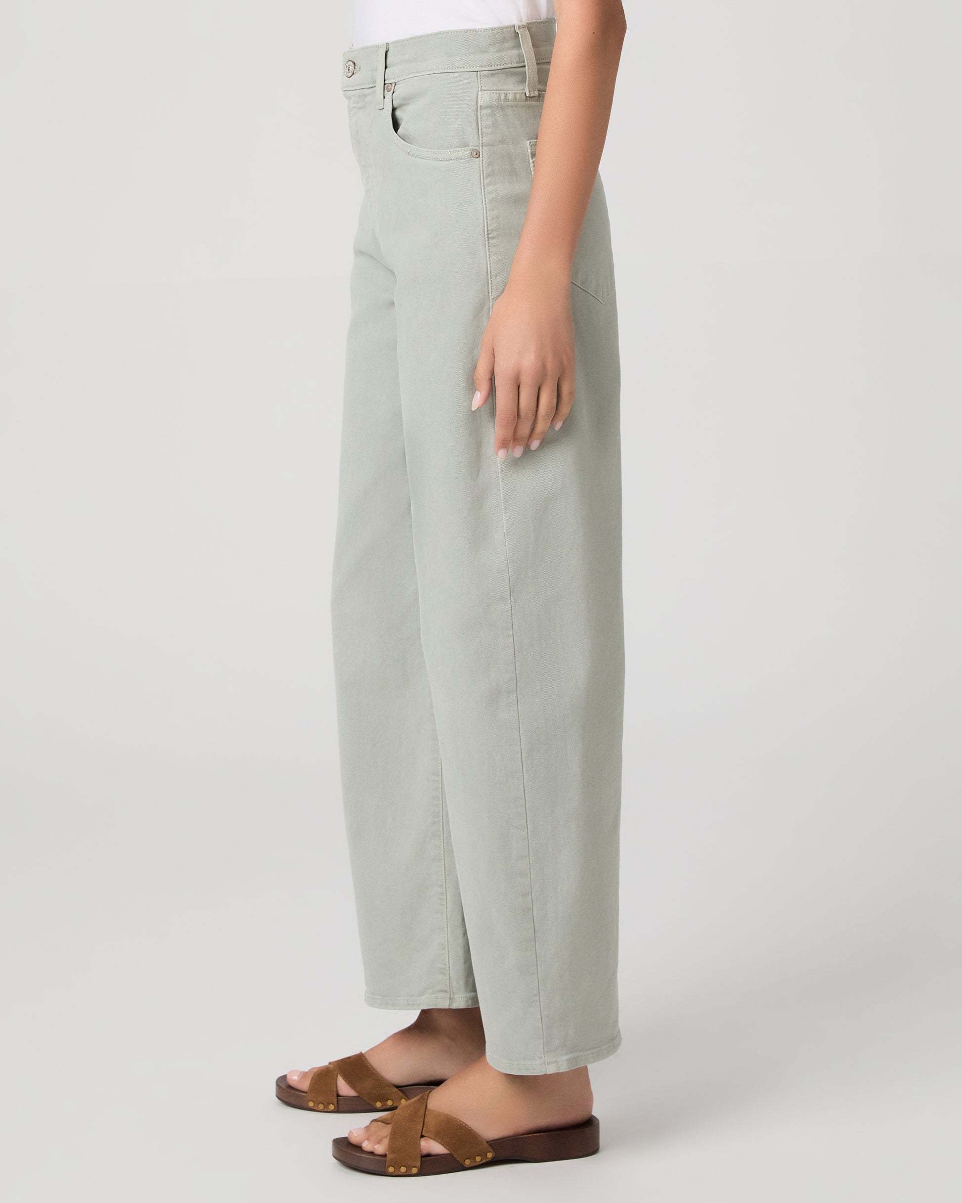 Woman wearing a white t-shirt and light green pants paired with brown sandals on a white background