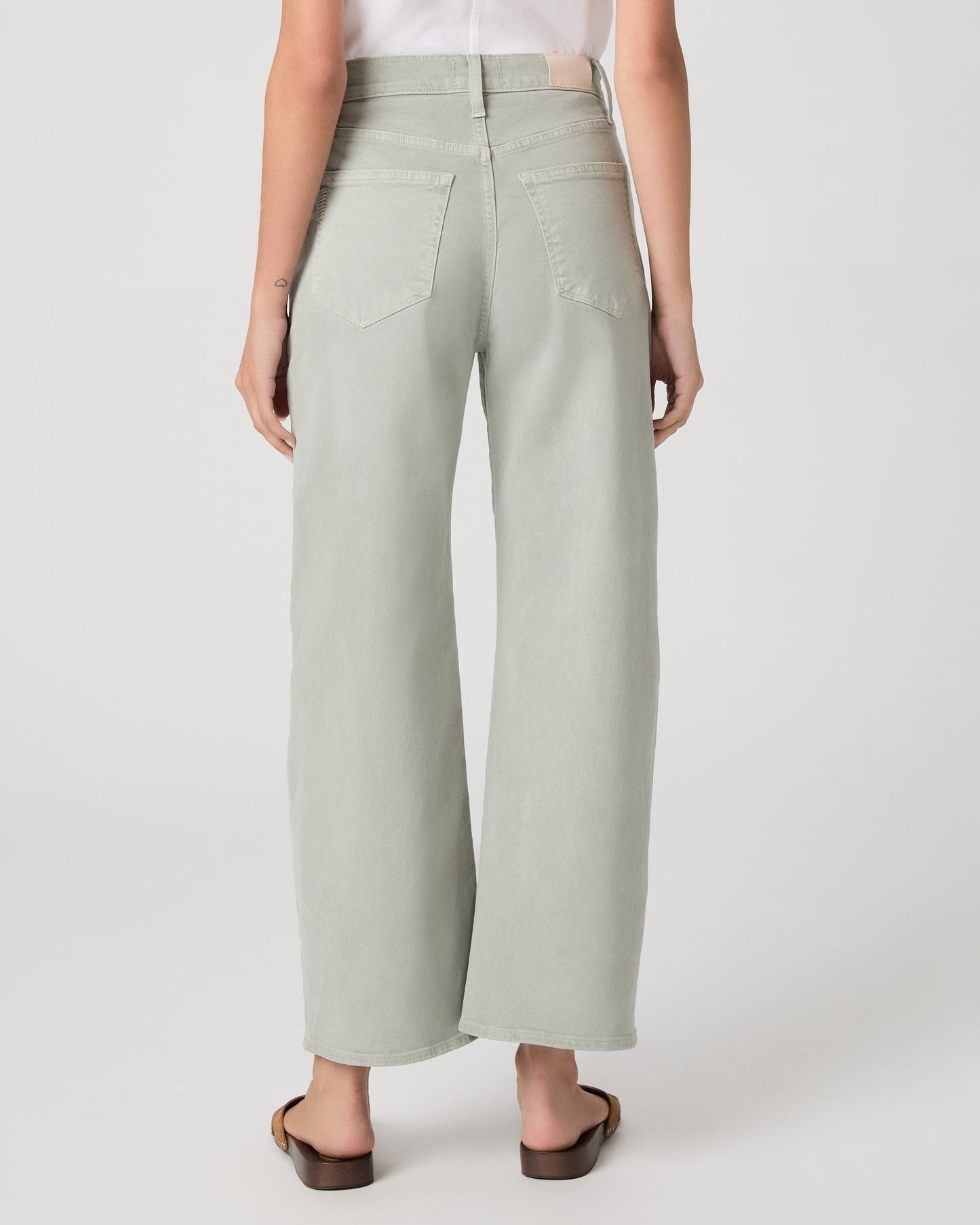 Woman wearing a white t-shirt and light green pants paired with brown sandals on a white background