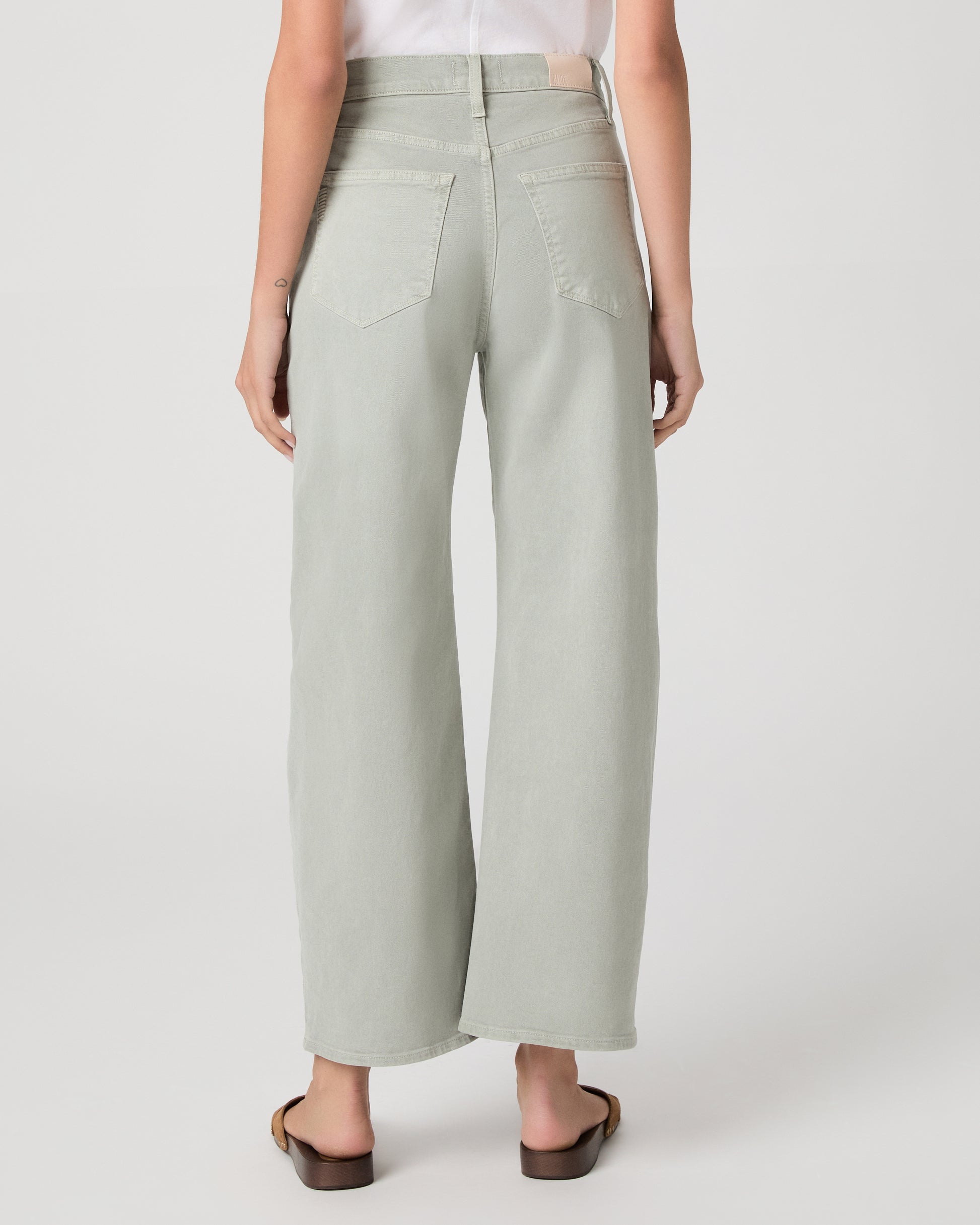 Woman wearing a white t-shirt and light green pants paired with brown sandals on a white background