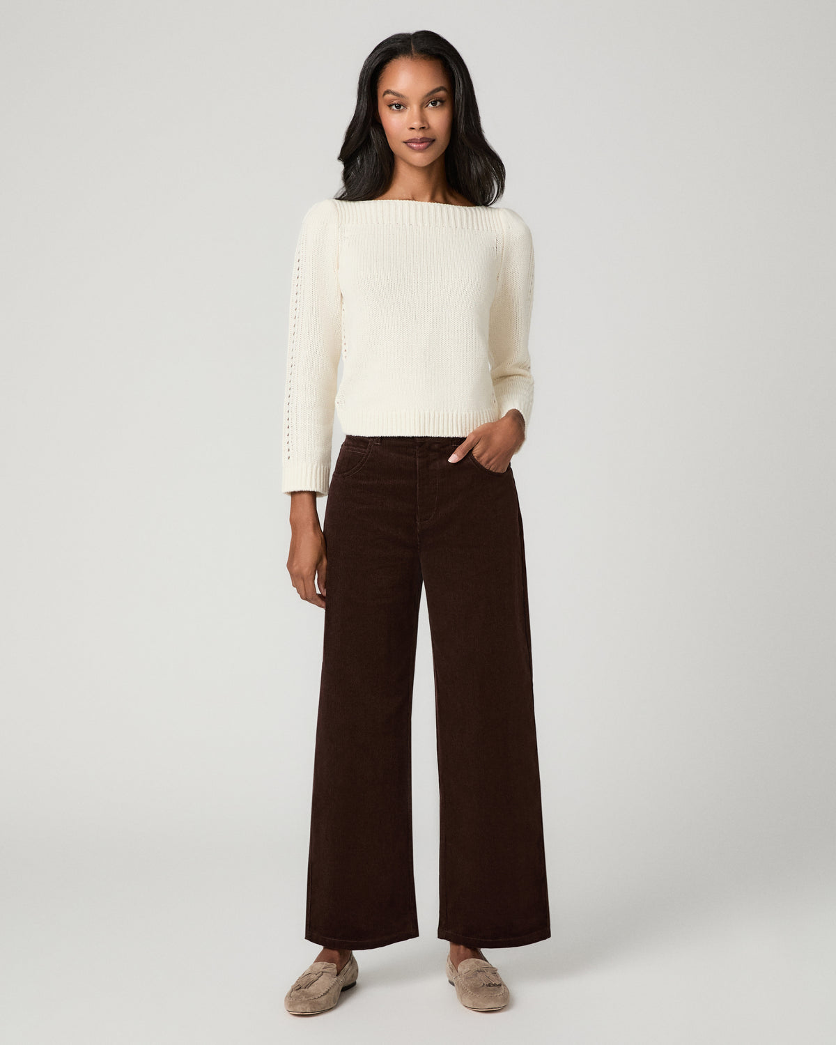 Women wearing a ivory long sleeve sweater paired with corduroy brown pant and grey flats against a white background