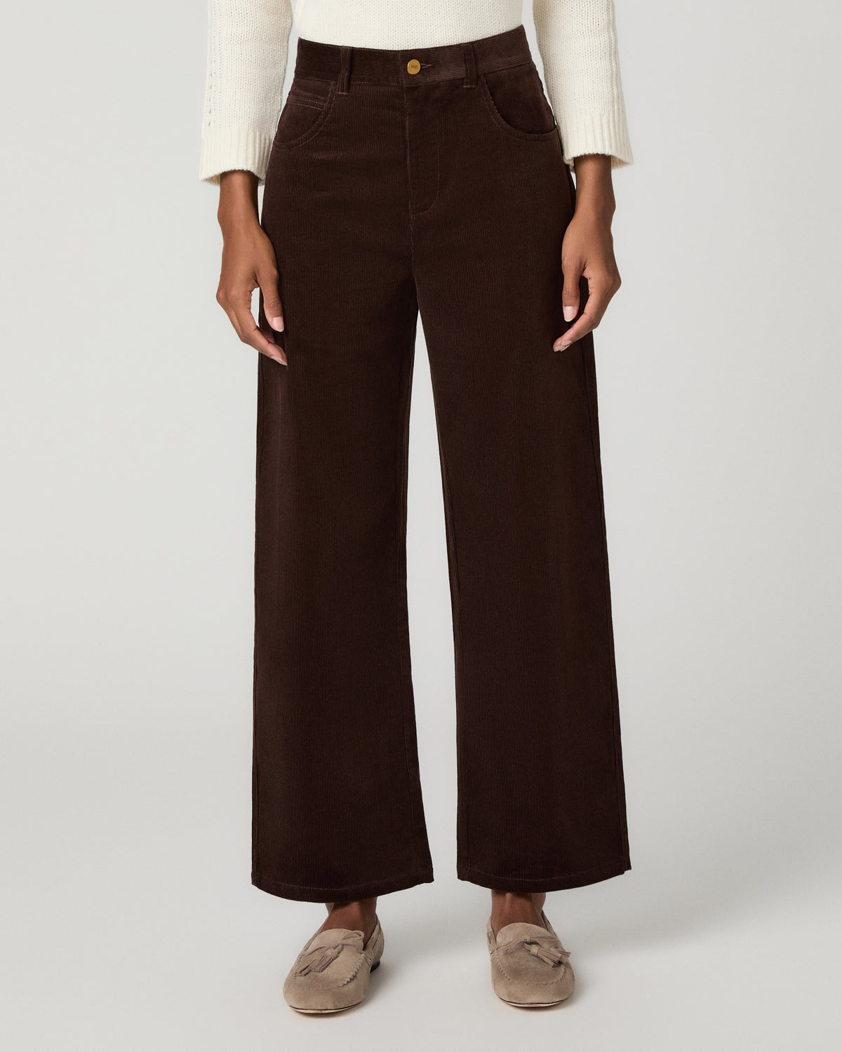 Women wearing a ivory long sleeve sweater paired with corduroy brown pant and grey flats against a white background