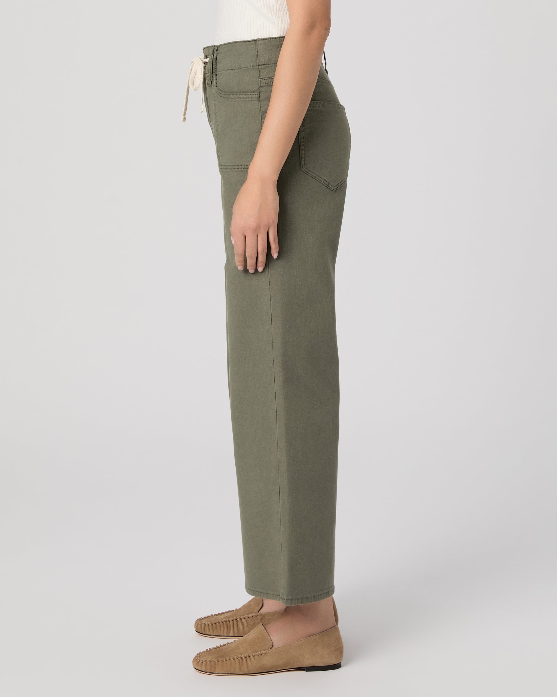 Woman wearing a white sleeveless top and green pants paired with brown flats on a white background