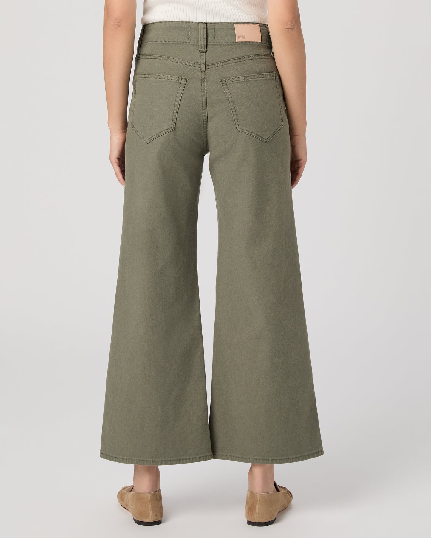 Woman wearing a white sleeveless top and green pants paired with brown flats on a white background