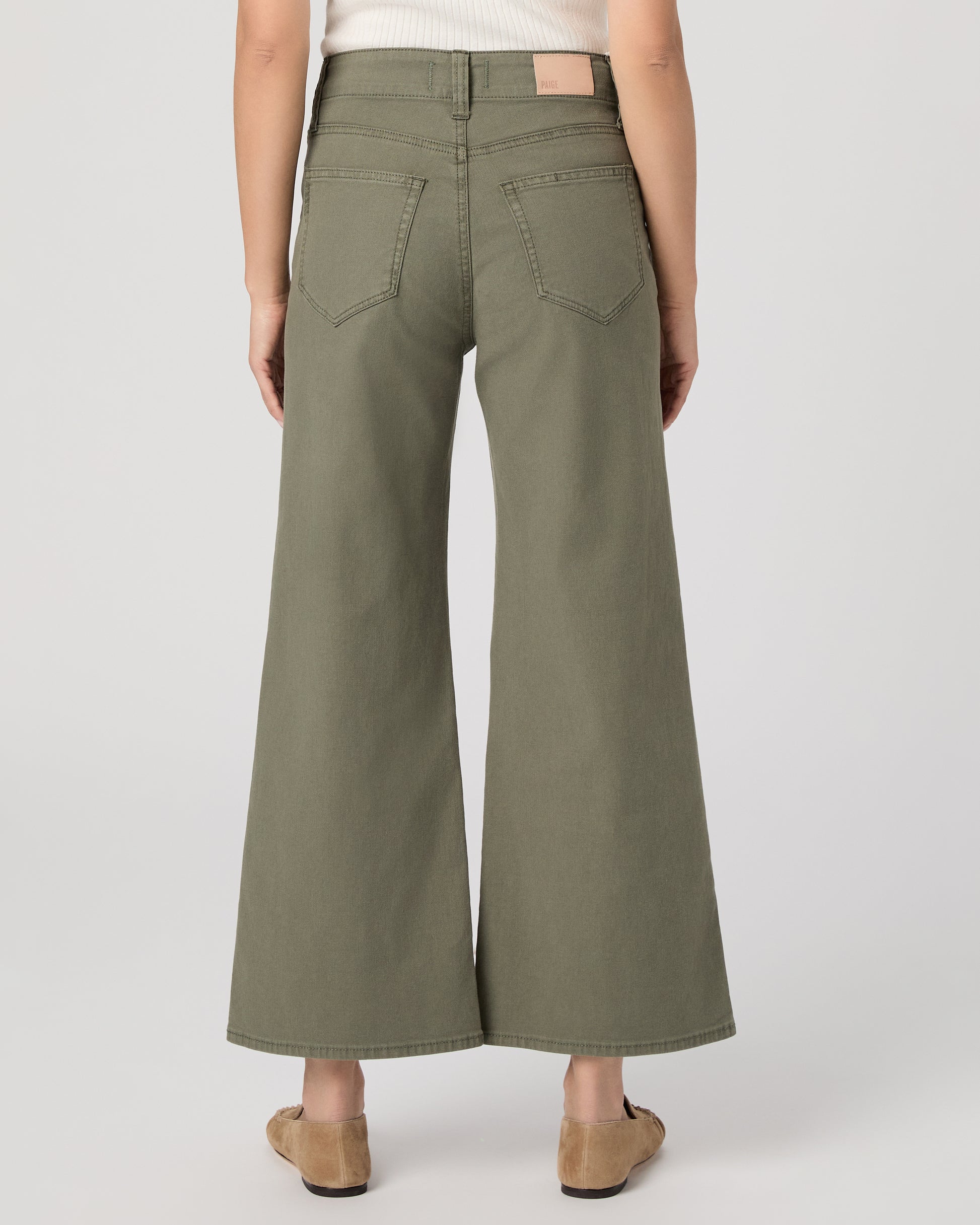 Woman wearing a white sleeveless top and green pants paired with brown flats on a white background