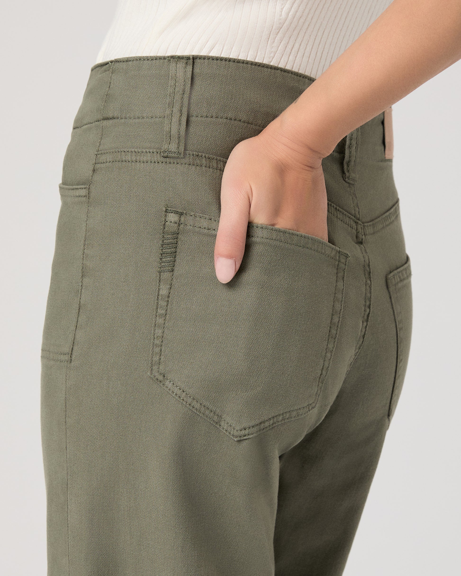 Woman wearing a white sleeveless top and green pants paired with brown flats on a white background
