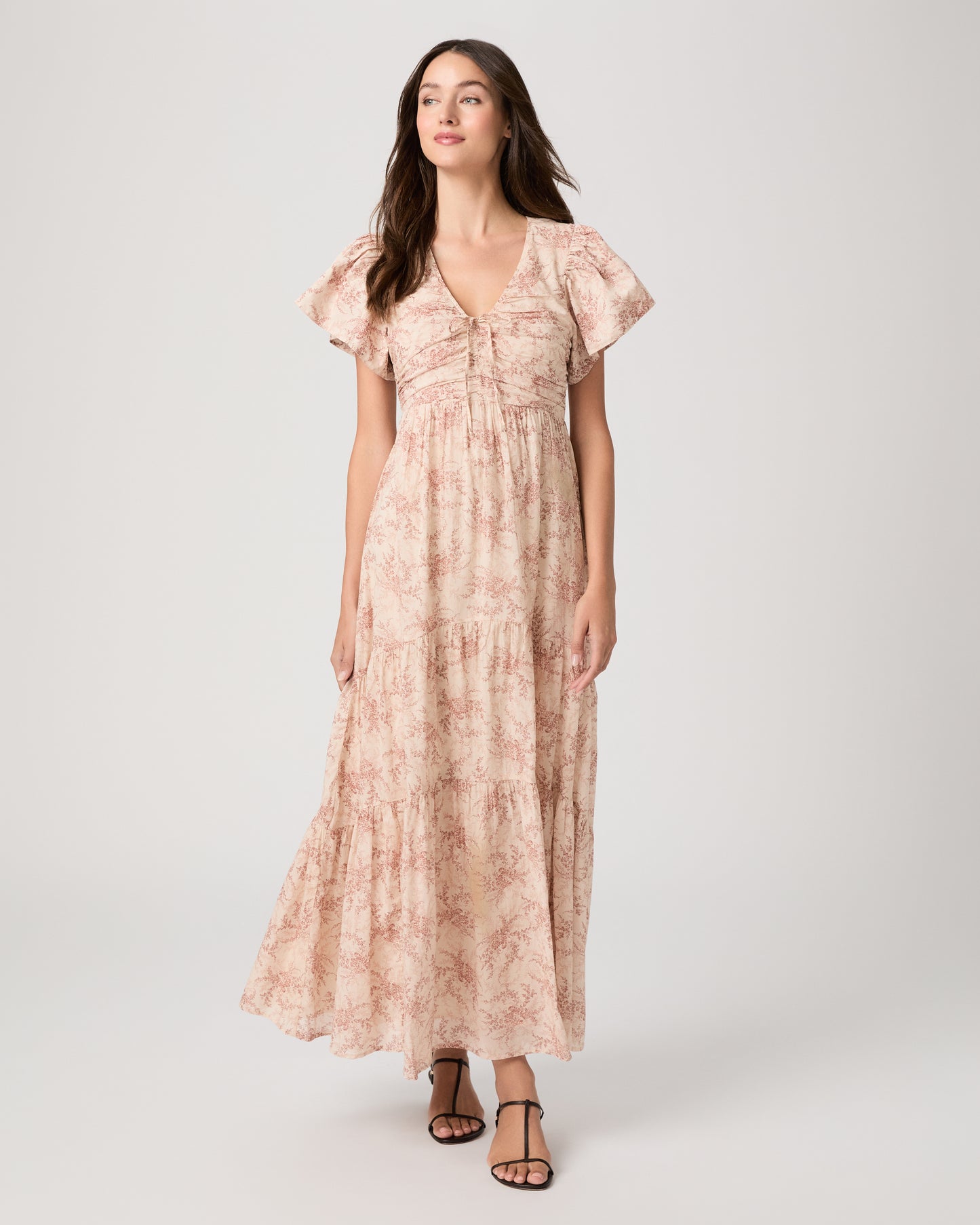 Woman wearing a long, patterned pink dress paired with black sandals on a white background