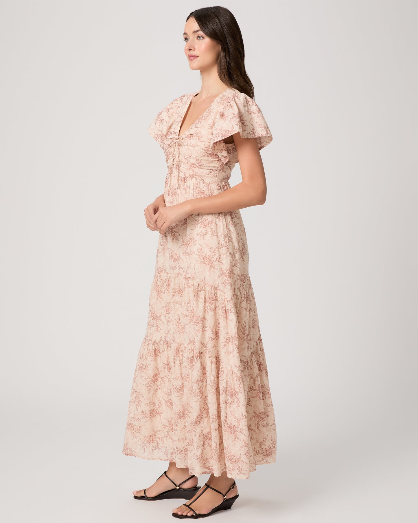 Woman wearing a long, patterned pink dress paired with black sandals on a white background