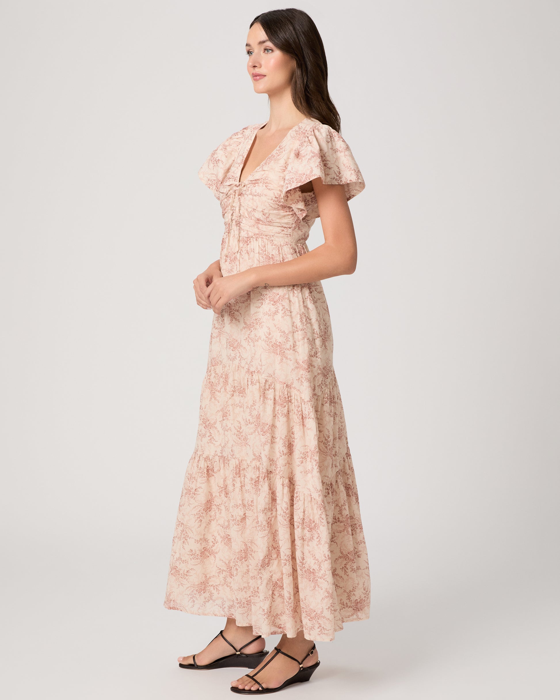 Woman wearing a long, patterned pink dress paired with black sandals on a white background