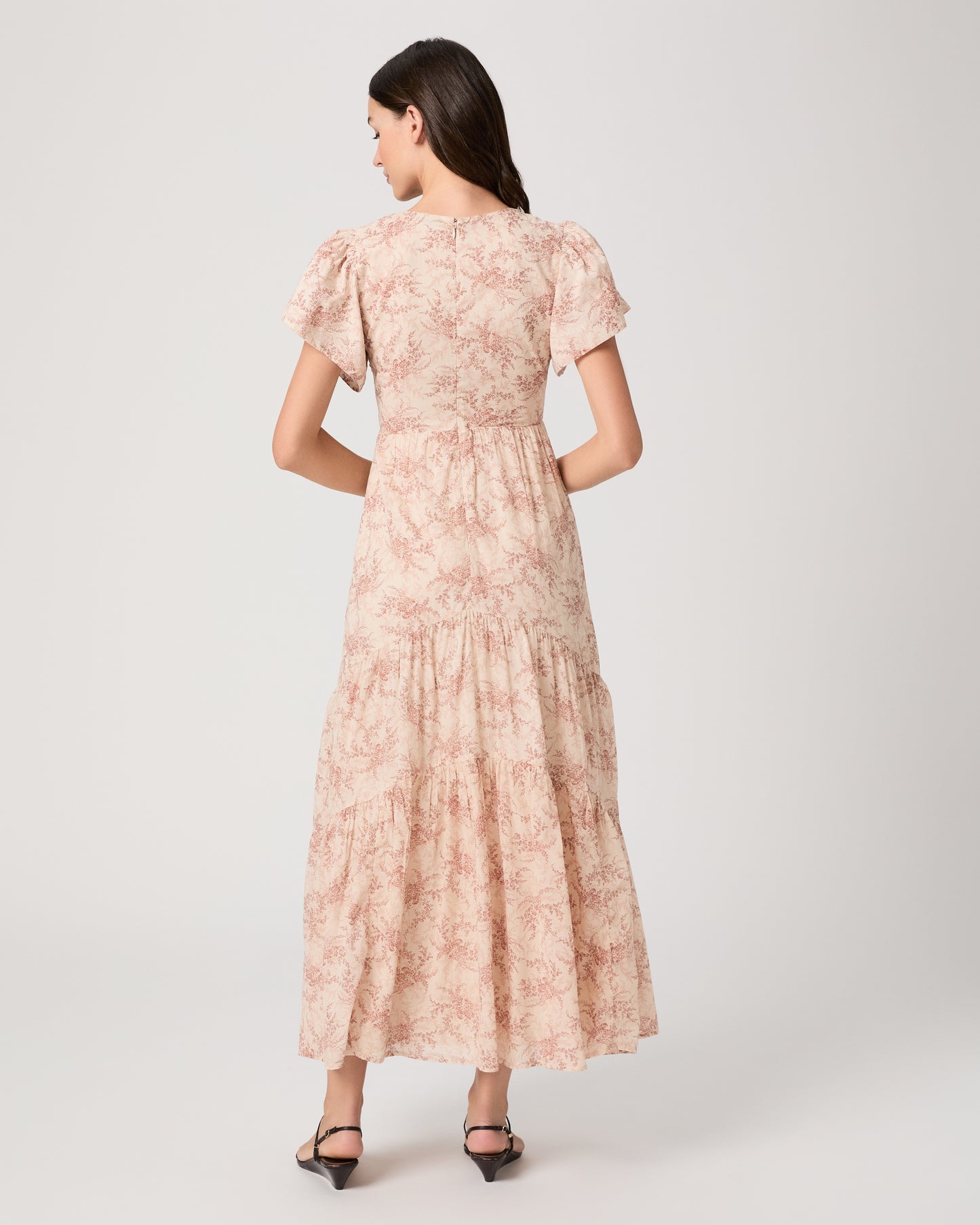 Woman wearing a long, patterned pink dress paired with black sandals on a white background