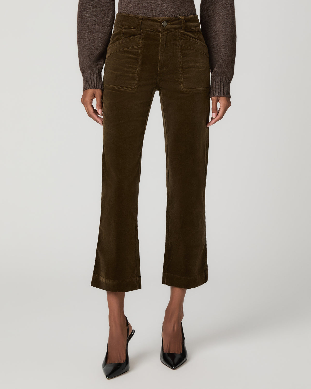 Close-up front view of fern green corduroy ankle pants with angled patch pockets and a button waistband, paired with black pointed-toe heels.
