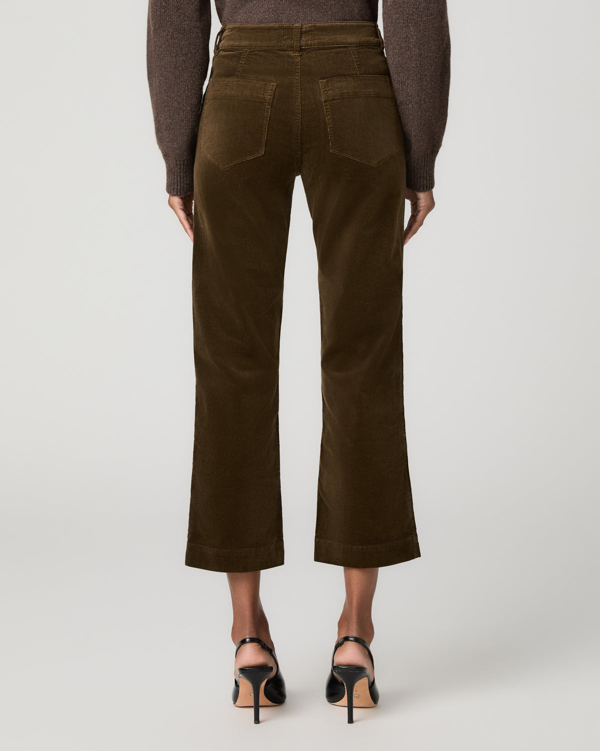 Close-up back view of fern green corduroy ankle pants showing back patch pockets, paired with black ankle-strap heels.