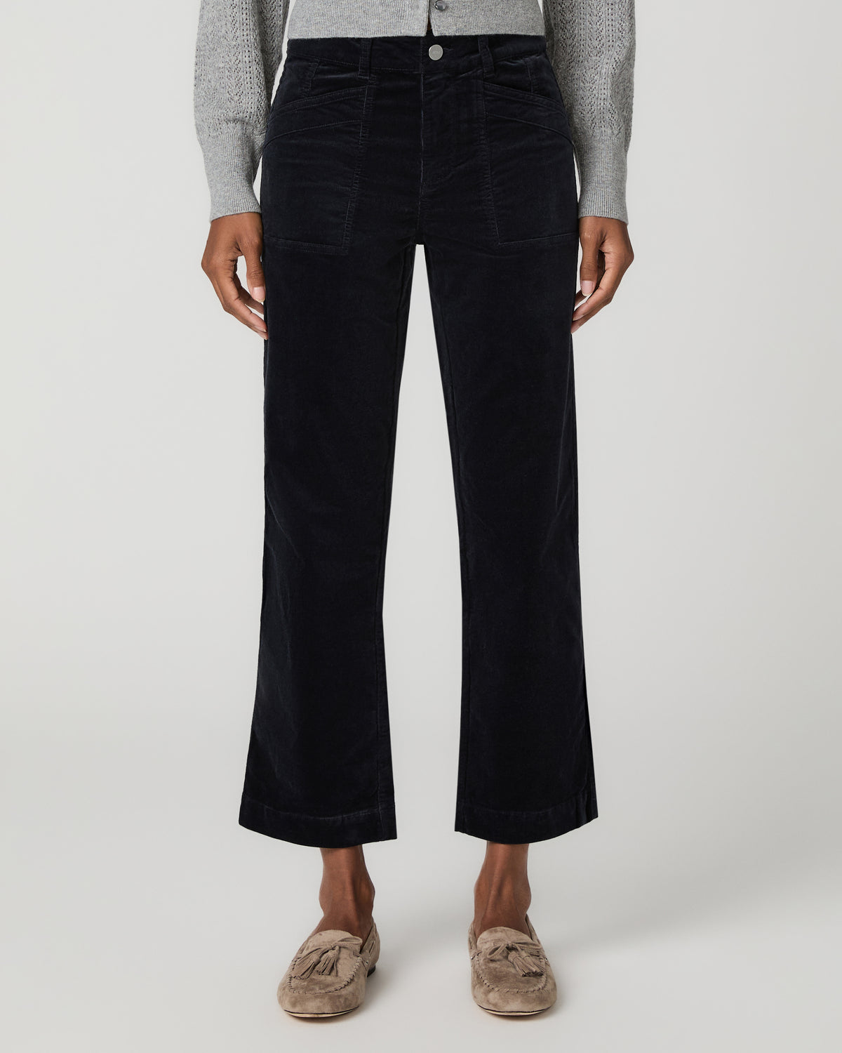 Close-up front view of navy corduroy ankle pants with angled patch pockets and a button waistband, paired with tan mule flats.