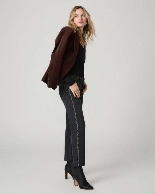 Front view of a woman wearing the washed black Mason Ankle Straight Jean with a black top and a brown suede jacket draped over her shoulders.