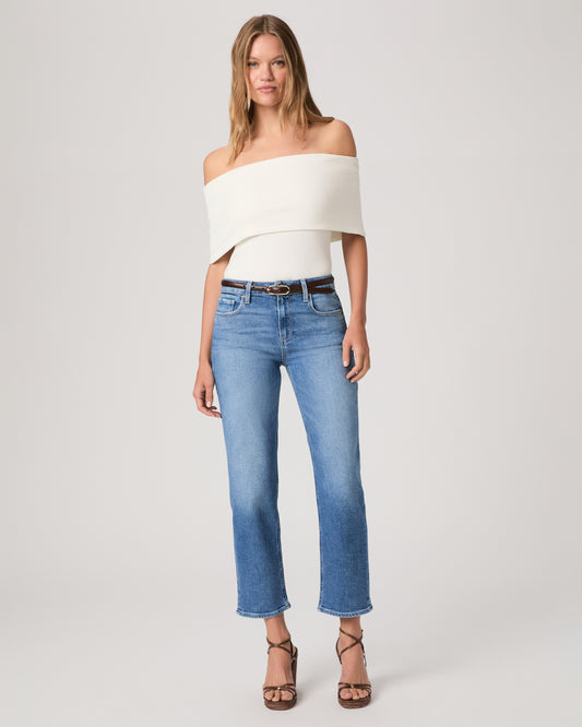 Woman wearing a white top paired with medium wash denim and brown heels against a white background