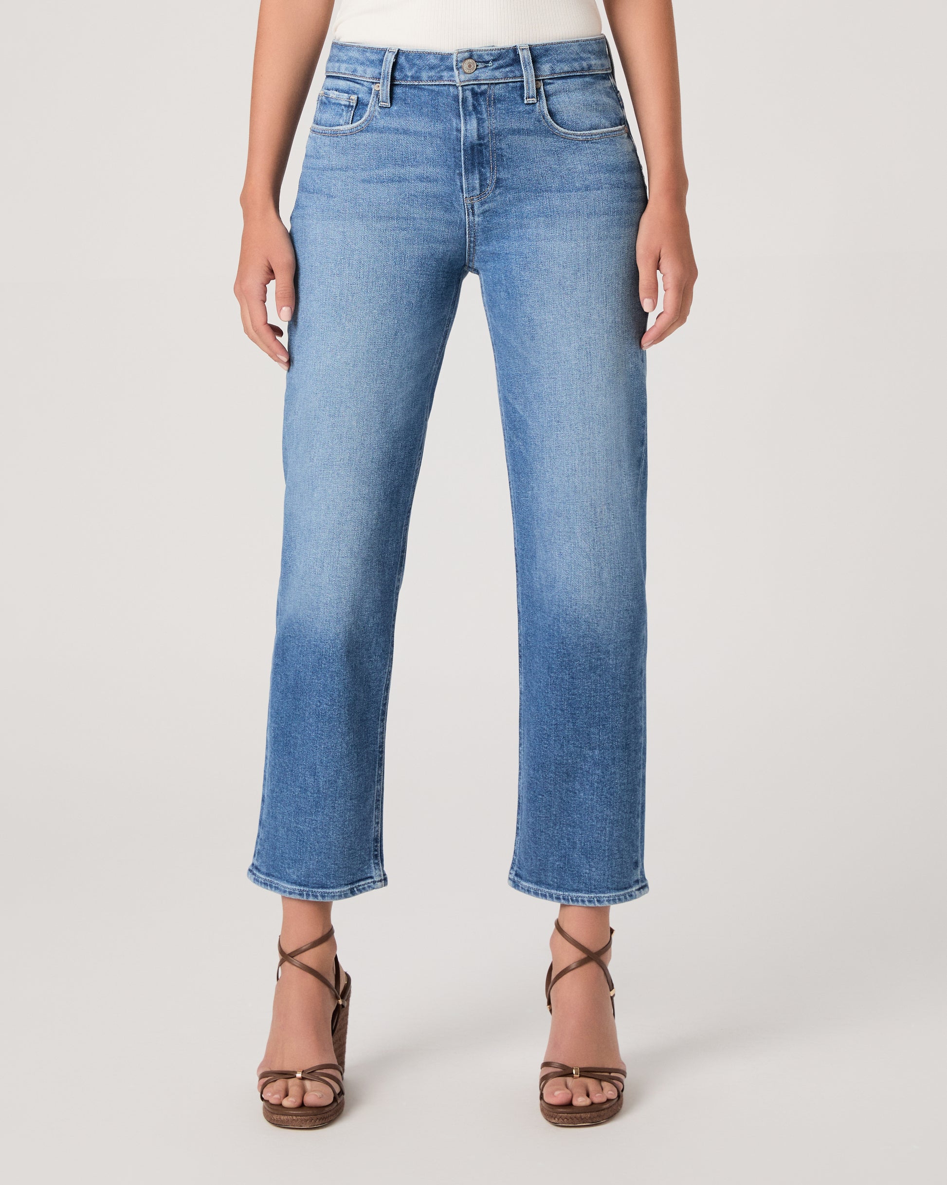 Woman wearing a white top paired with medium wash denim and brown heels against a white background