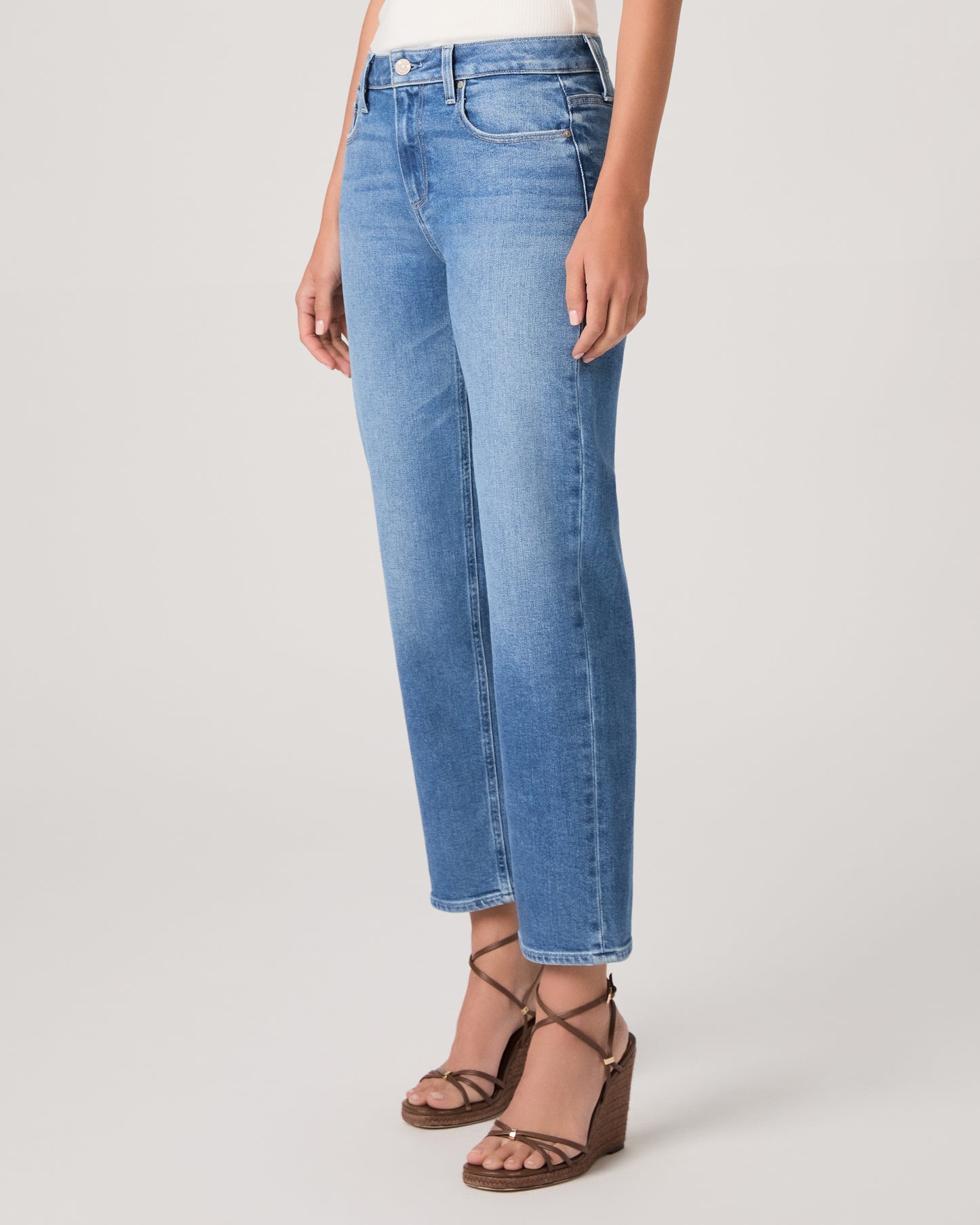 Woman wearing a white top paired with medium wash denim and brown heels against a white background