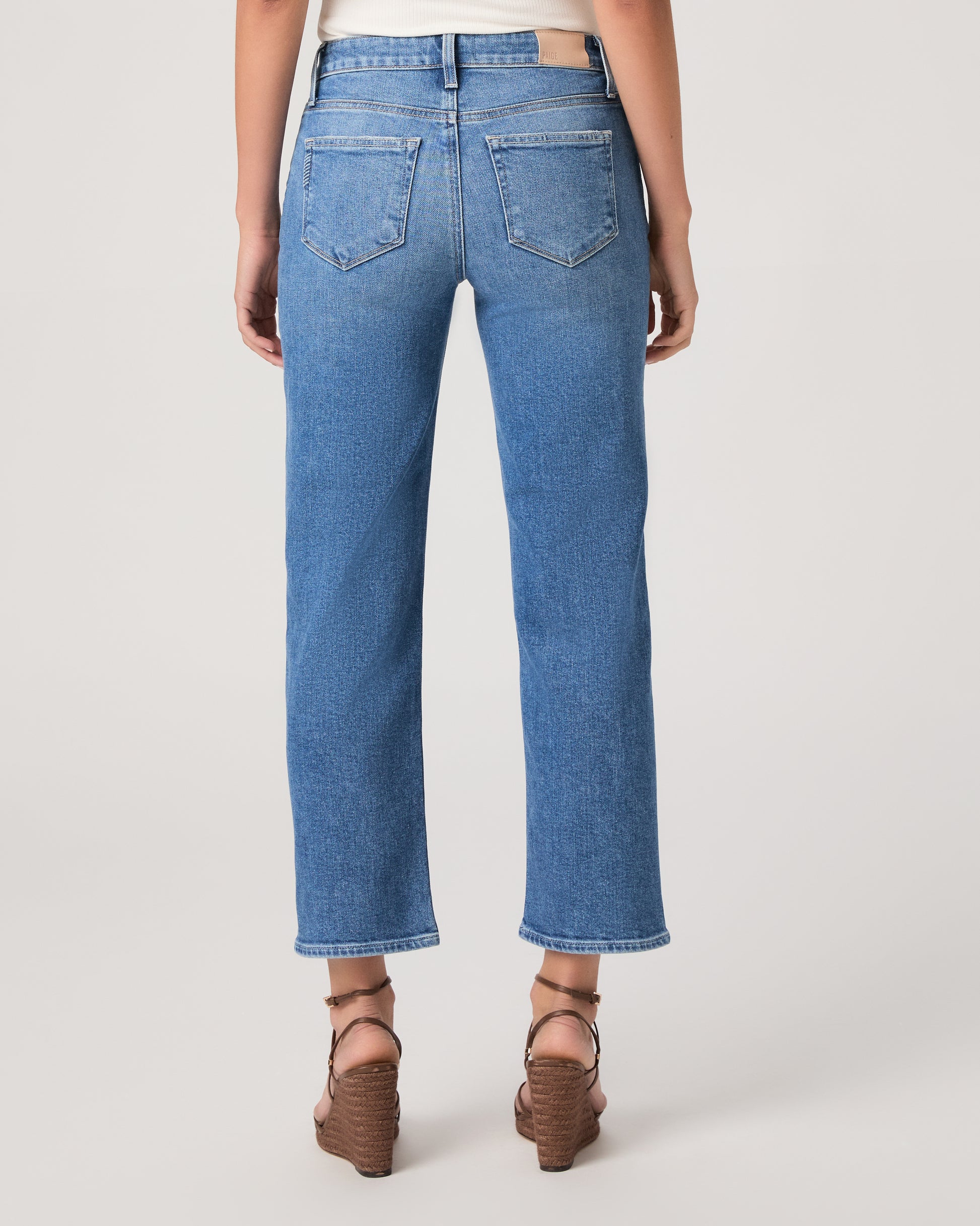 Woman wearing a white top paired with medium wash denim and brown heels against a white background