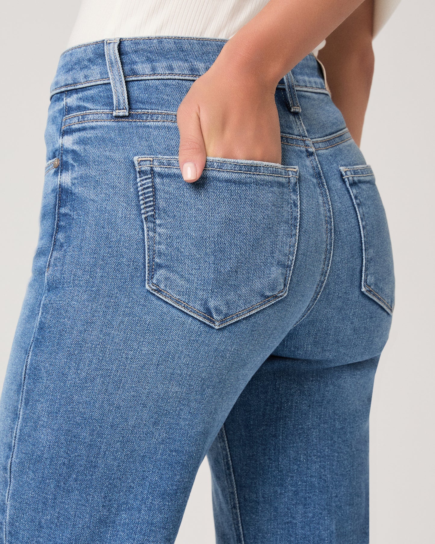 Woman wearing a white top paired with medium wash denim and brown heels against a white background
