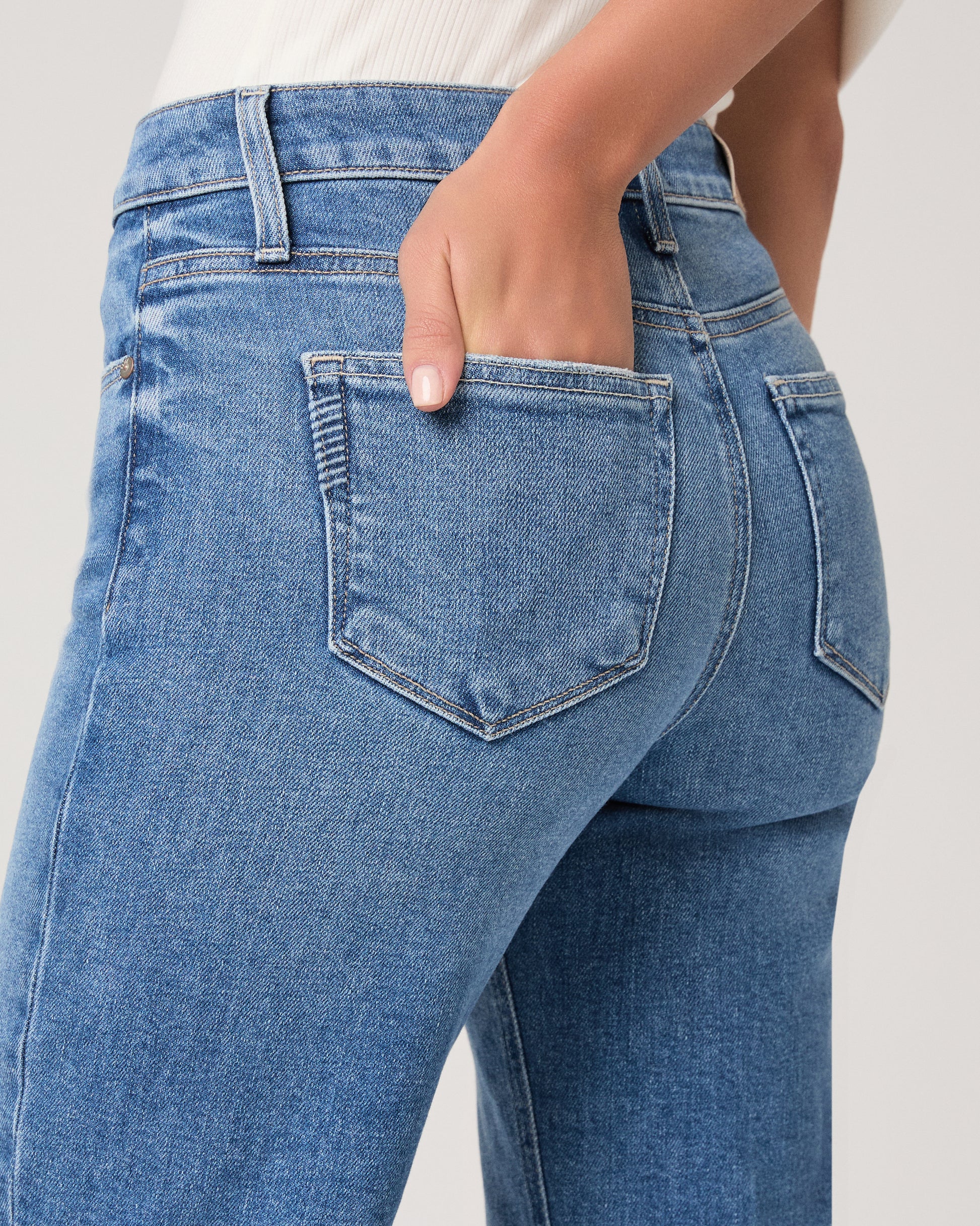 Woman wearing a white top paired with medium wash denim and brown heels against a white background