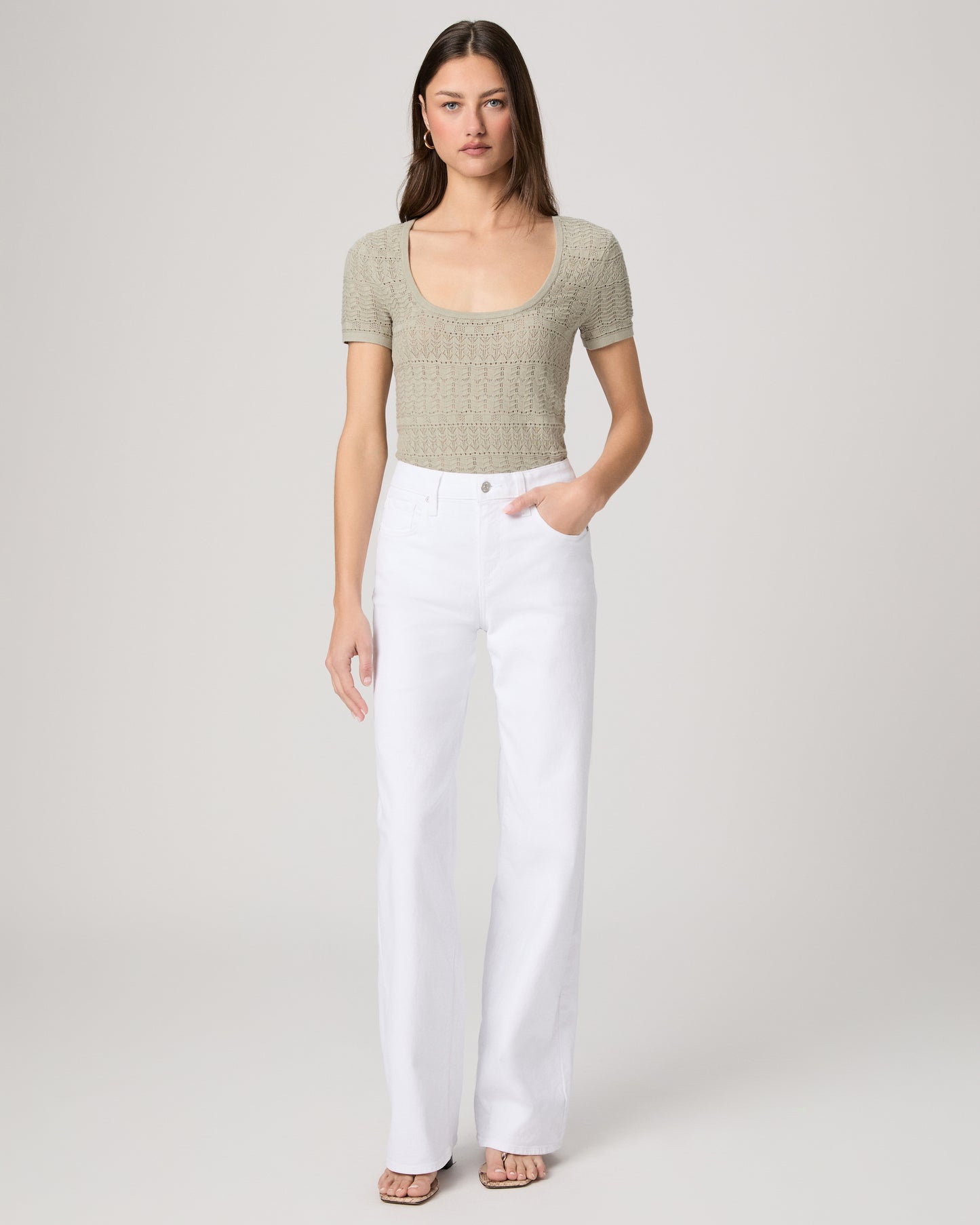 Woman wearing a green top and white pants on a plain background