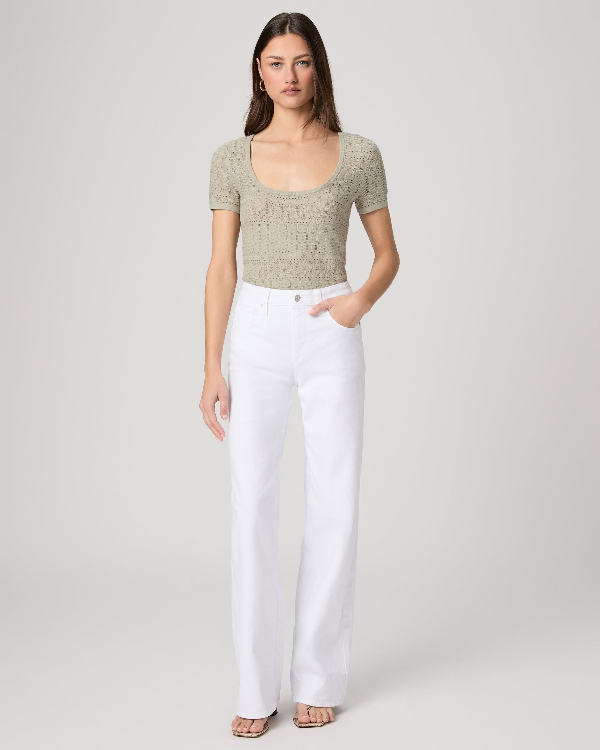 Woman wearing a green top and white pants on a plain background