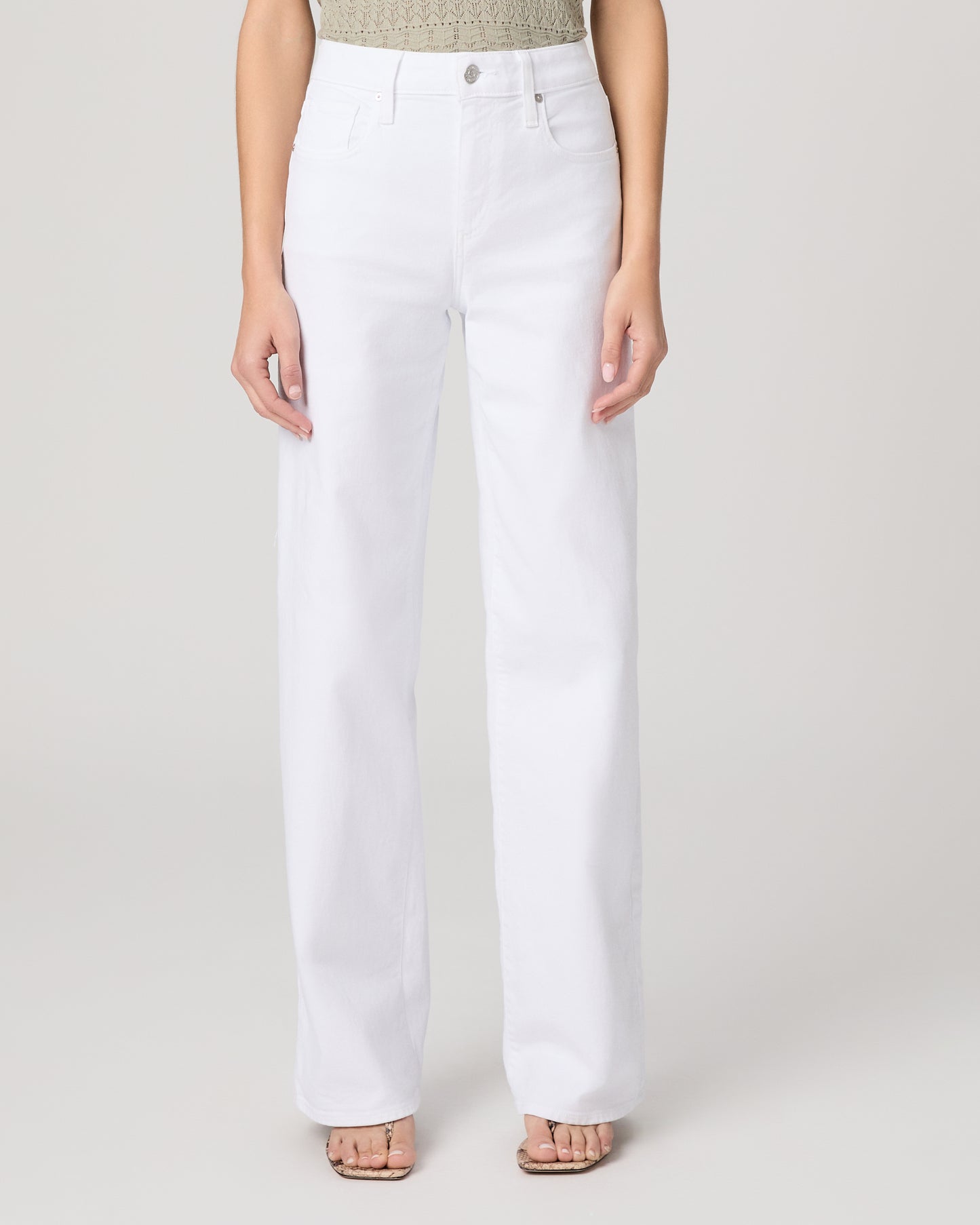 Woman wearing a green top and white pants on a plain background