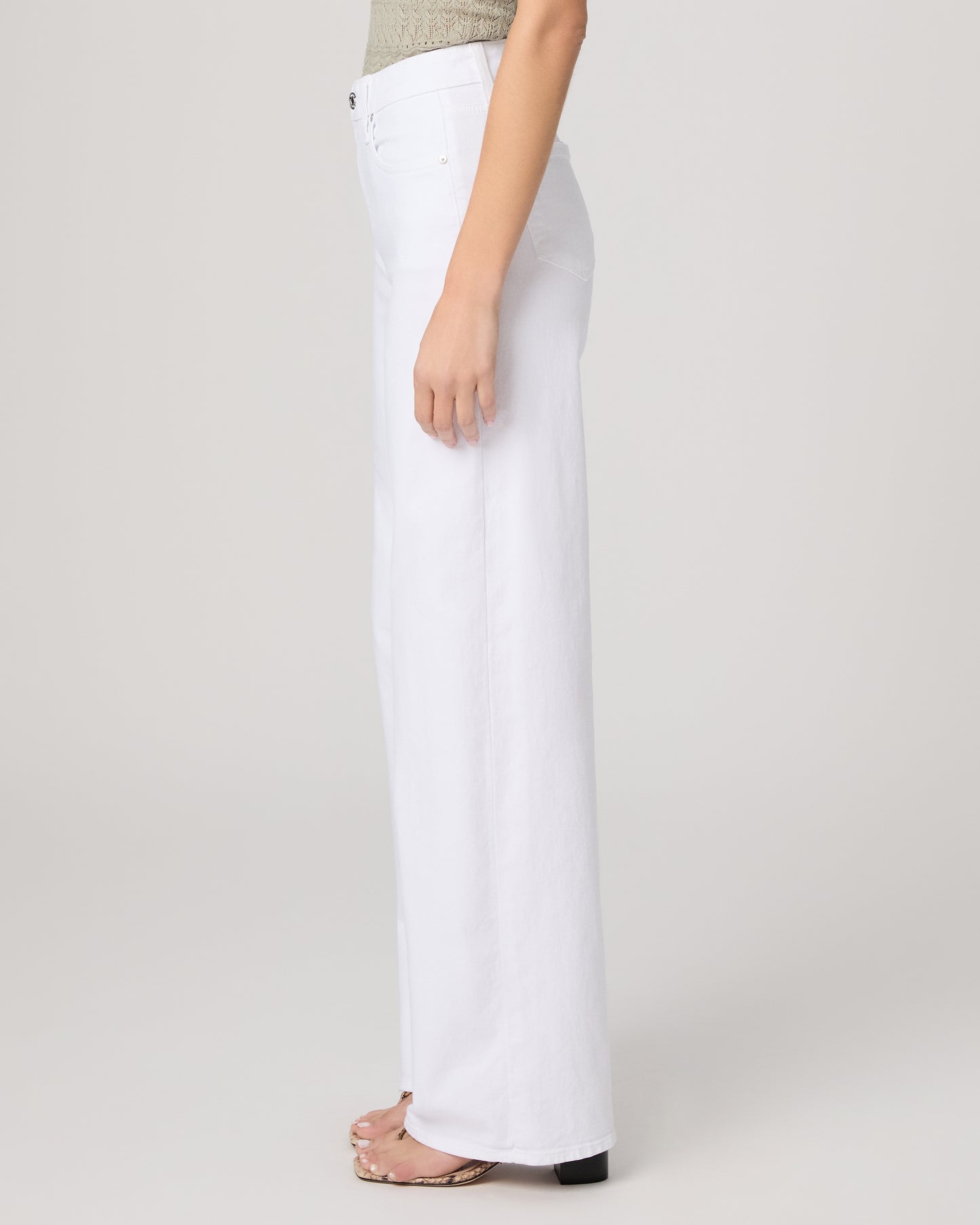 Woman wearing a green top and white pants on a plain background
