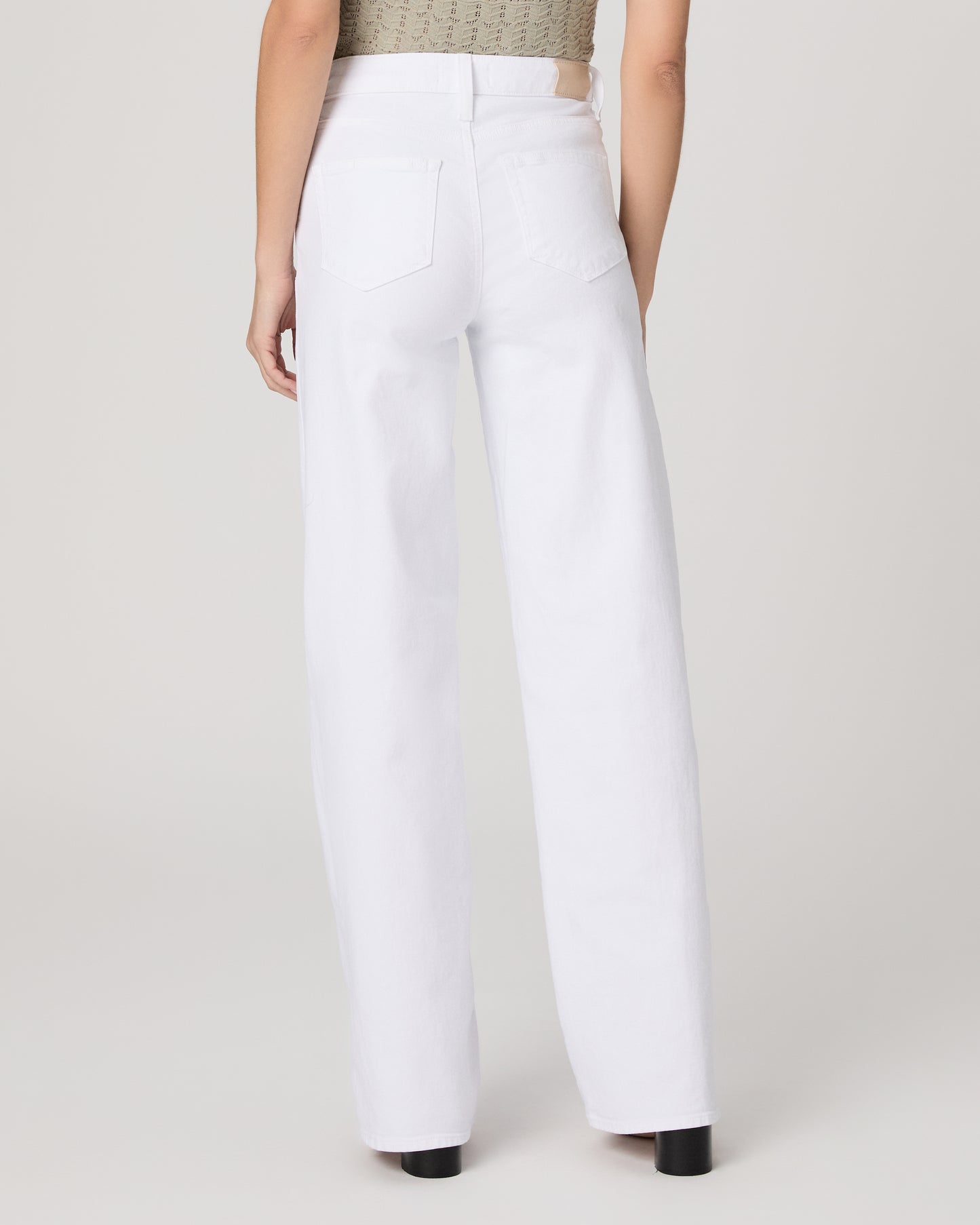 Woman wearing a green top and white pants on a plain background