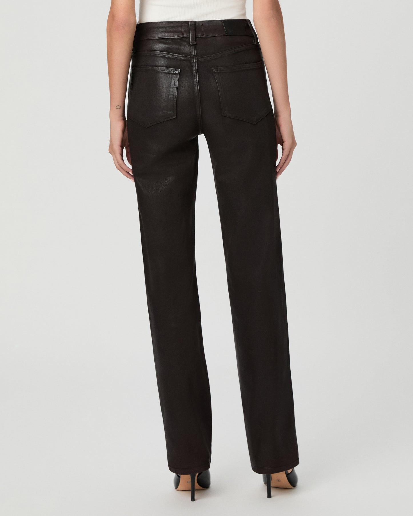 A woman modeling an off-the-shoulder white top and black straight-leg jeans against a light gray studio background.