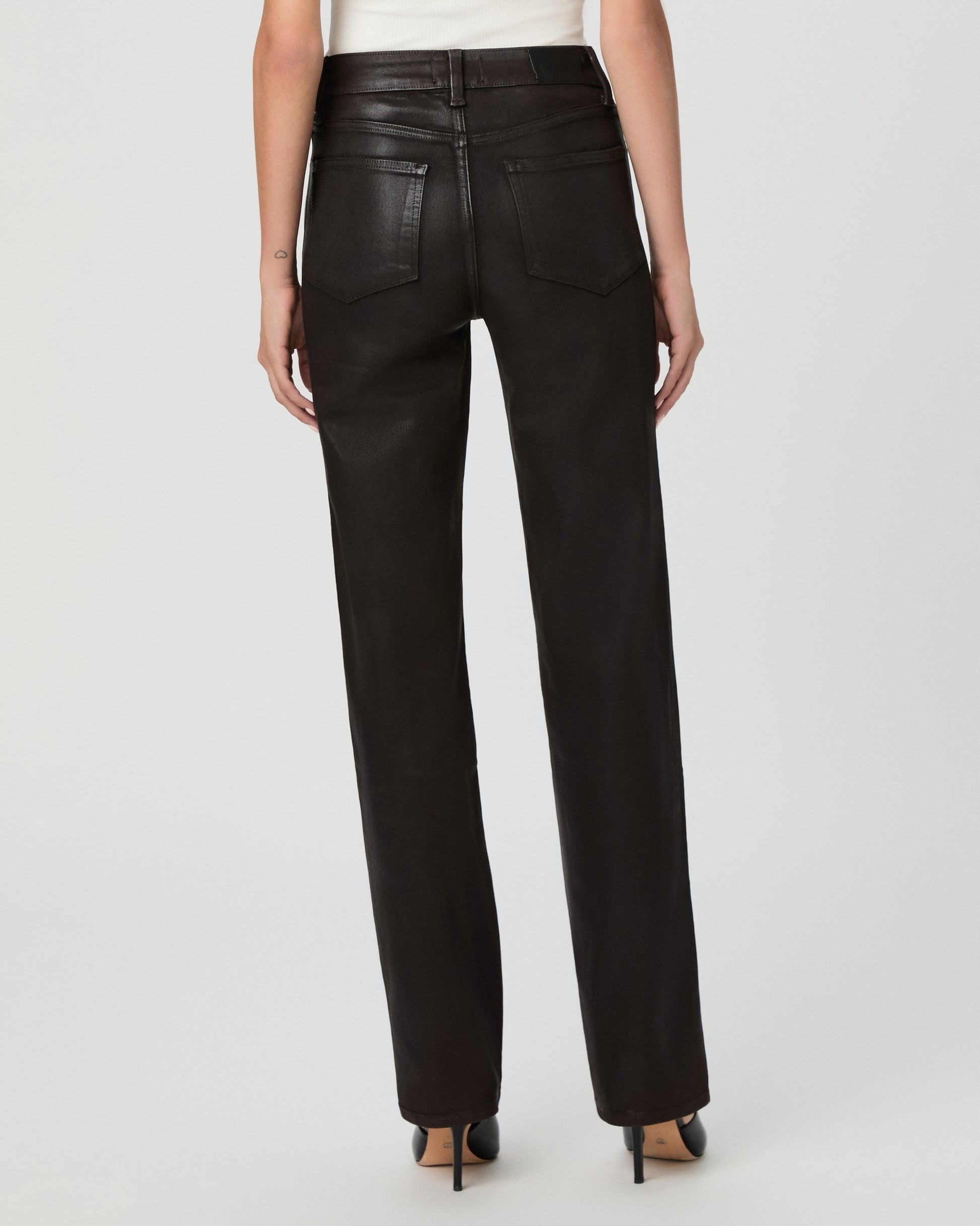 A woman modeling an off-the-shoulder white top and black straight-leg jeans against a light gray studio background.