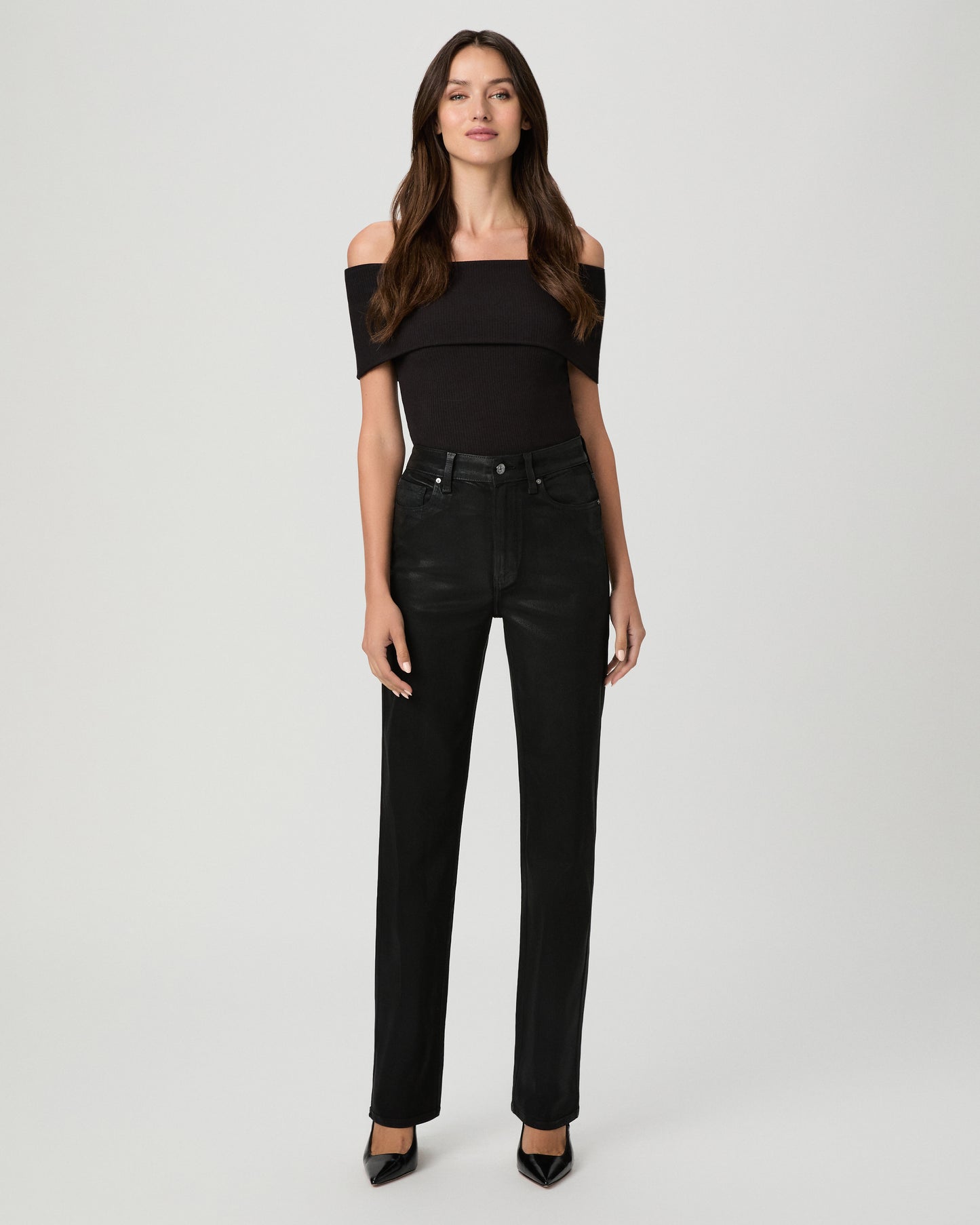 A woman modeling a black off-the-shoulder top and black high-waisted straight-leg jeans against a light gray studio background.