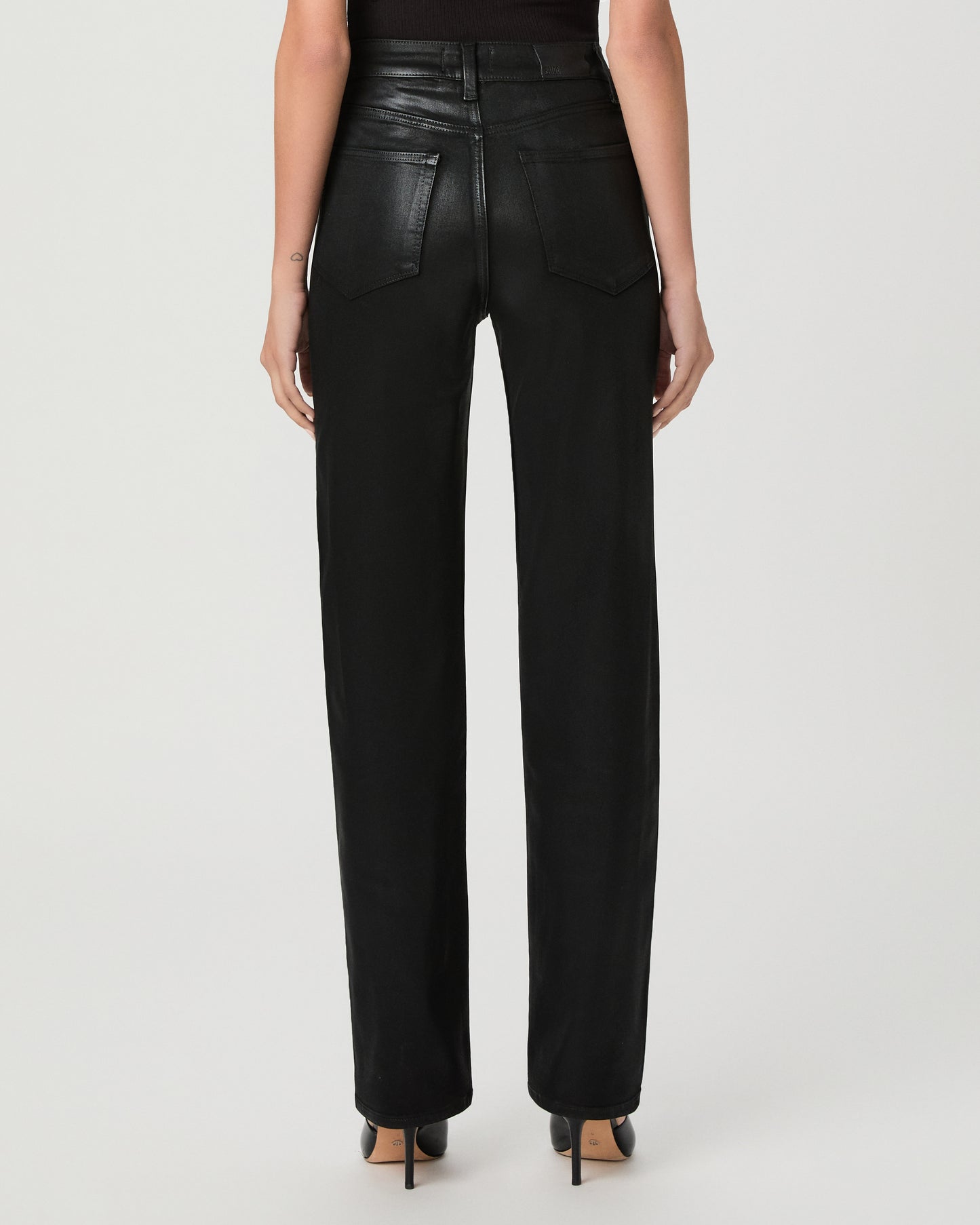 A woman modeling a black off-the-shoulder top and black high-waisted straight-leg jeans against a light gray studio background.