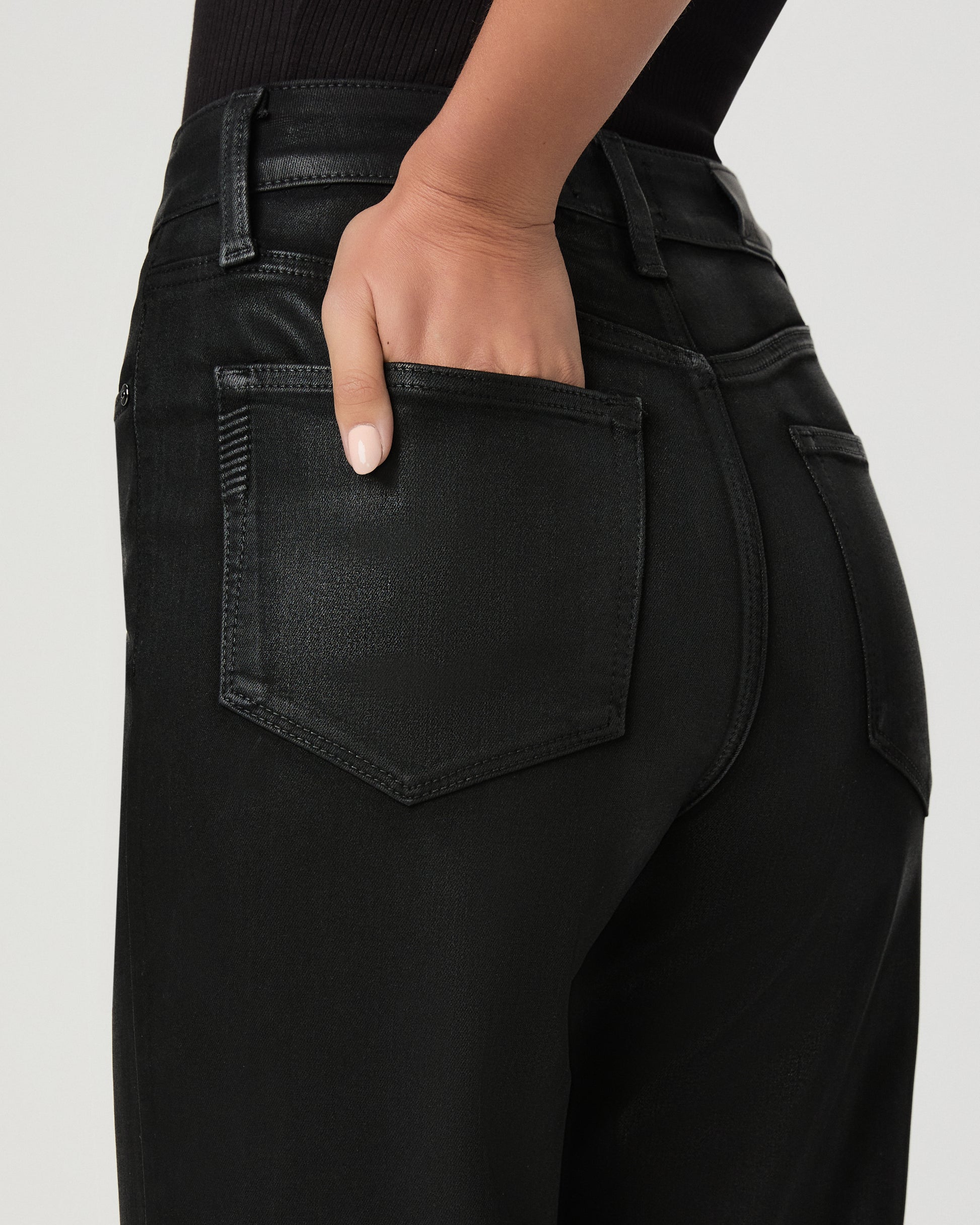 A woman modeling a black off-the-shoulder top and black high-waisted straight-leg jeans against a light gray studio background.