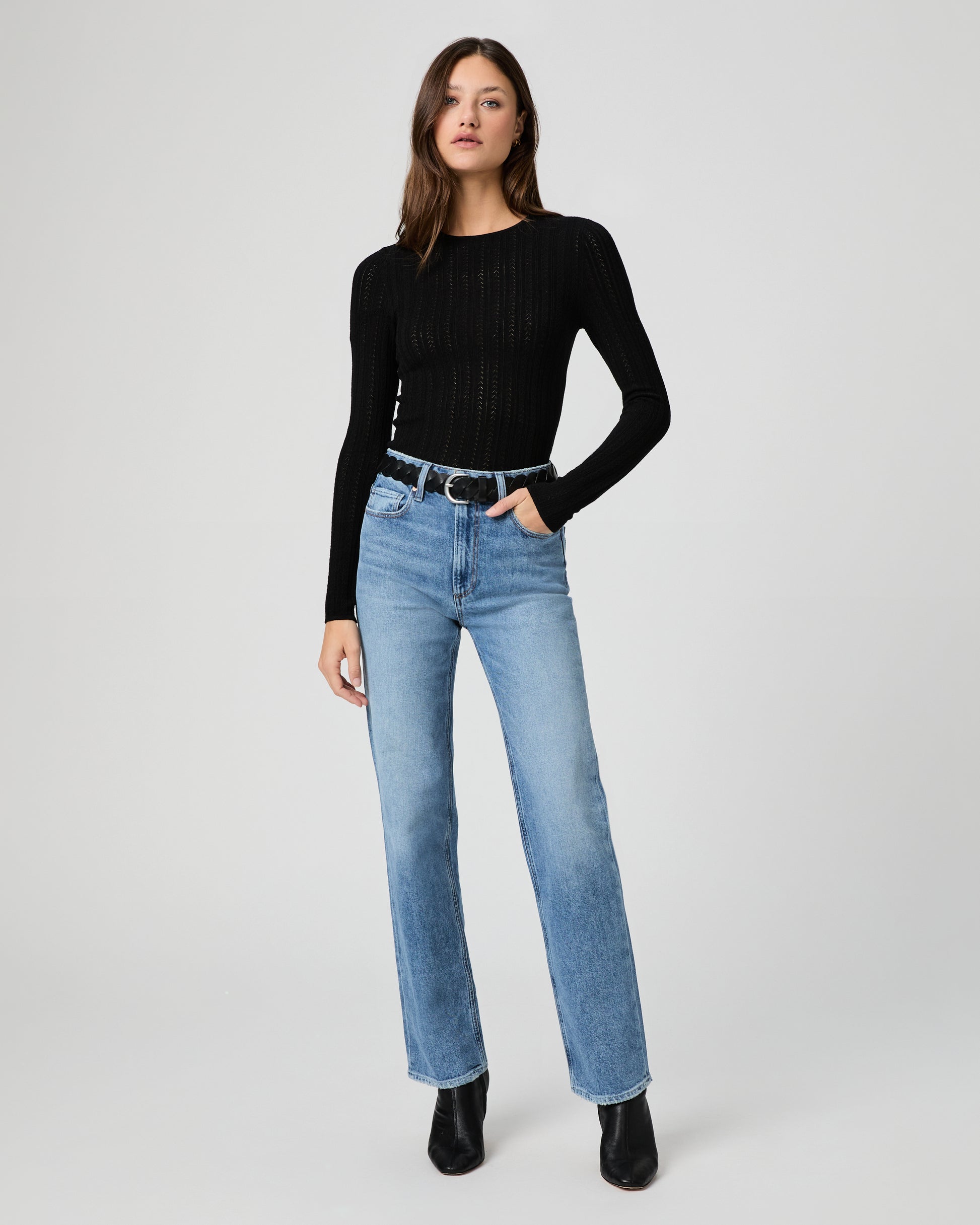 Woman wearing a black top and light blue jeans on a white background