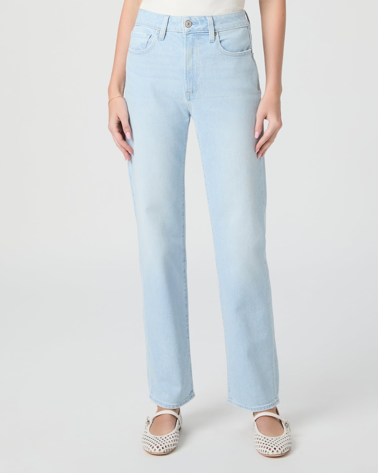 Woman wearing light blue jeans and a white off-shoulder top paired with white sandals on a white background
