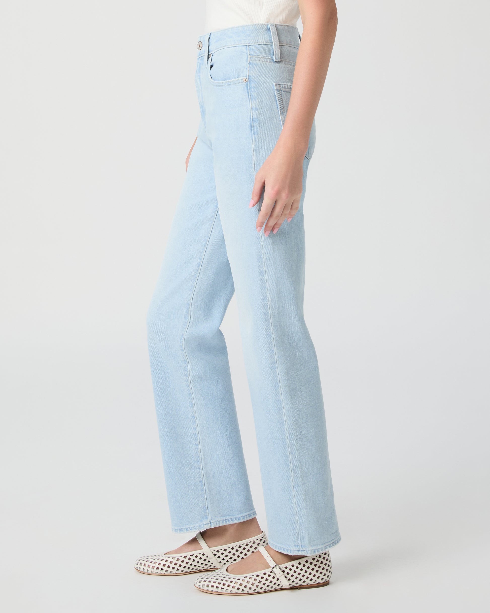 Woman wearing light blue jeans and a white off-shoulder top paired with white sandals on a white background