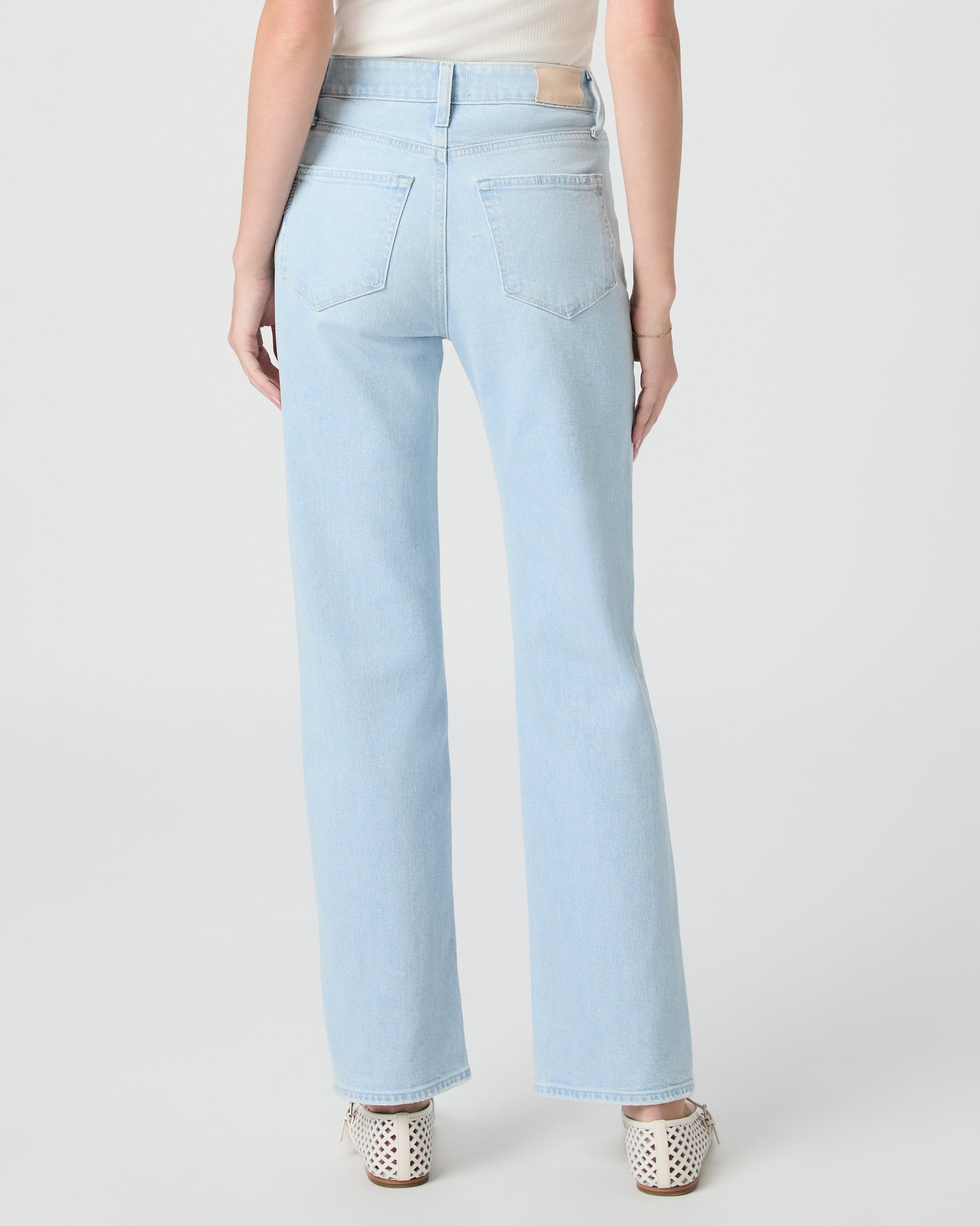 Woman wearing light blue jeans and a white off-shoulder top paired with white sandals on a white background